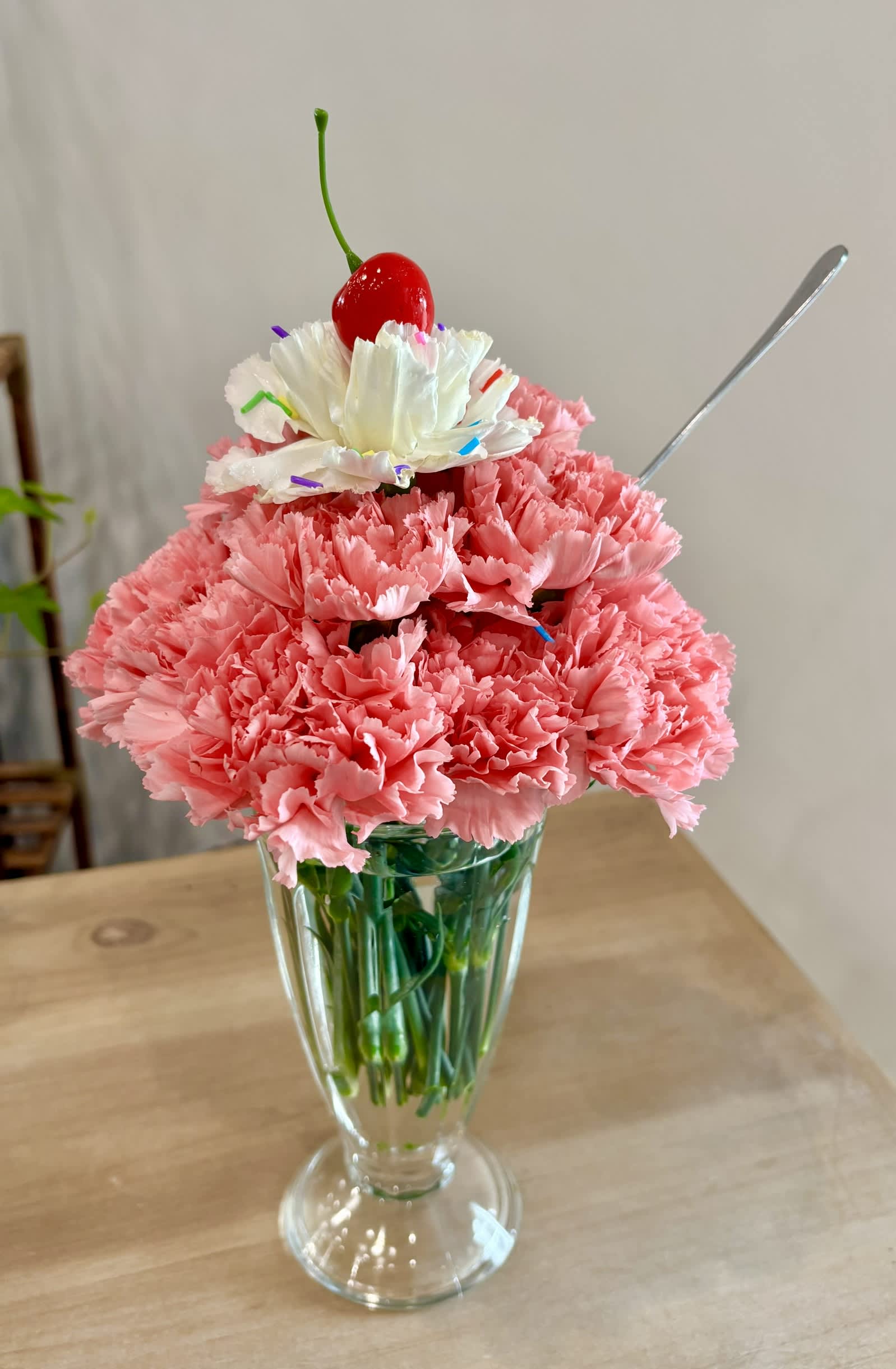 Pink carnations in a clear glass vase topped with a white flower and cherry