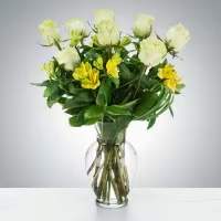 Glass vase of white roses and yellow alstroemeria in a rounded mixed bouquet