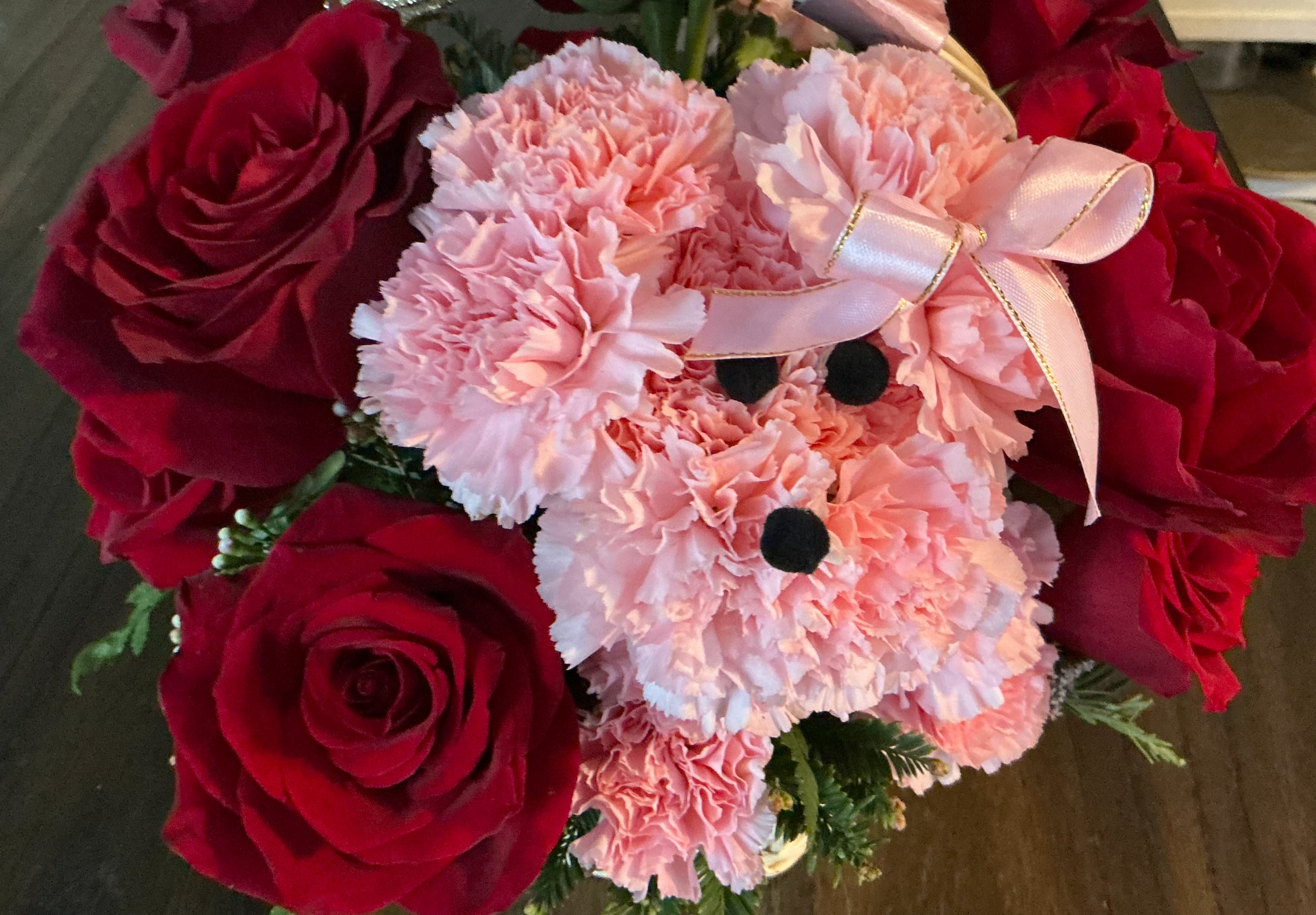 Pink teddy bear made of carnations surrounded by red roses