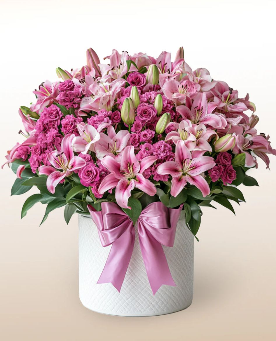 Pink lilies and roses arranged in a white hatbox with a pink ribbon