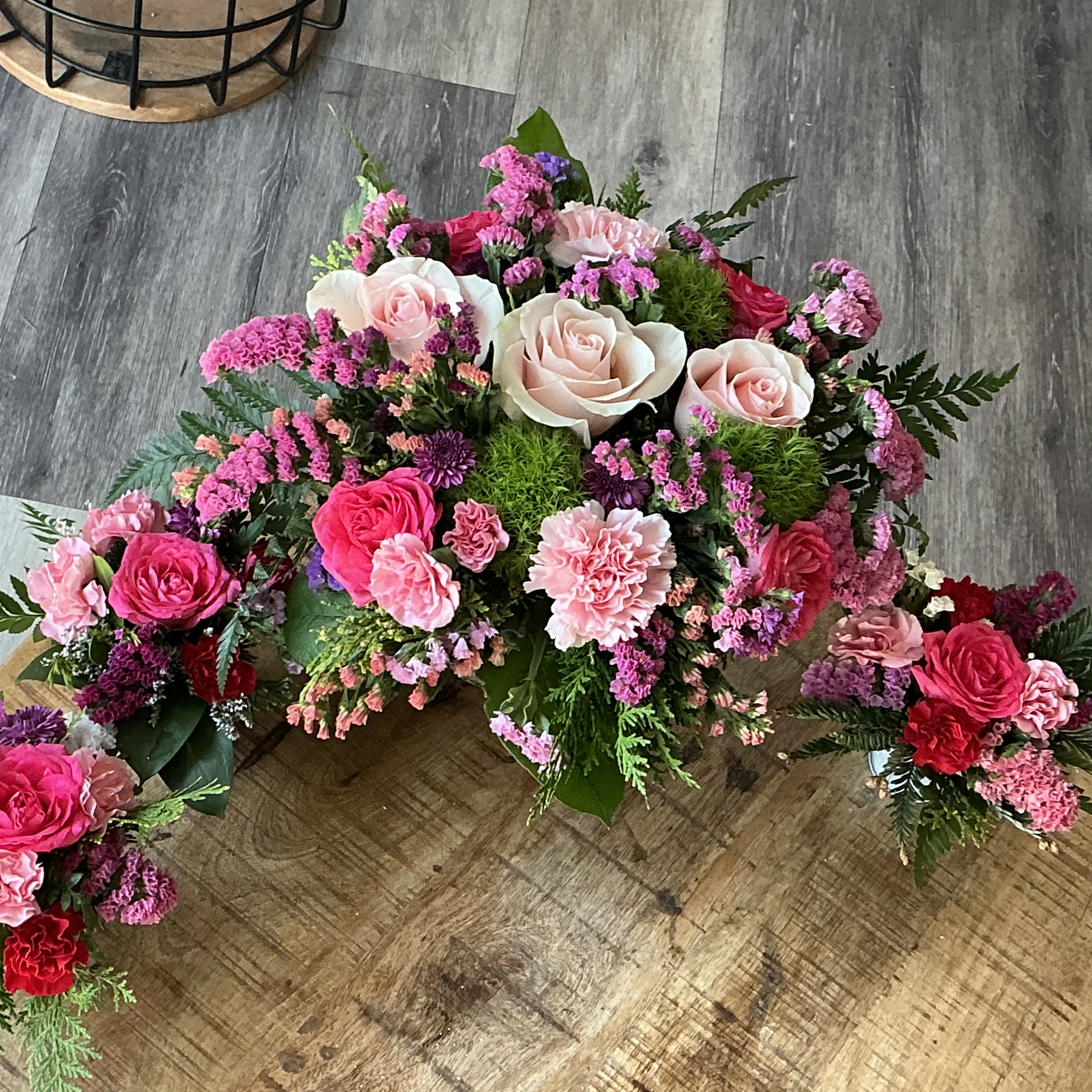 Pink and cream rose floral arrangement with carnations on a wooden floor