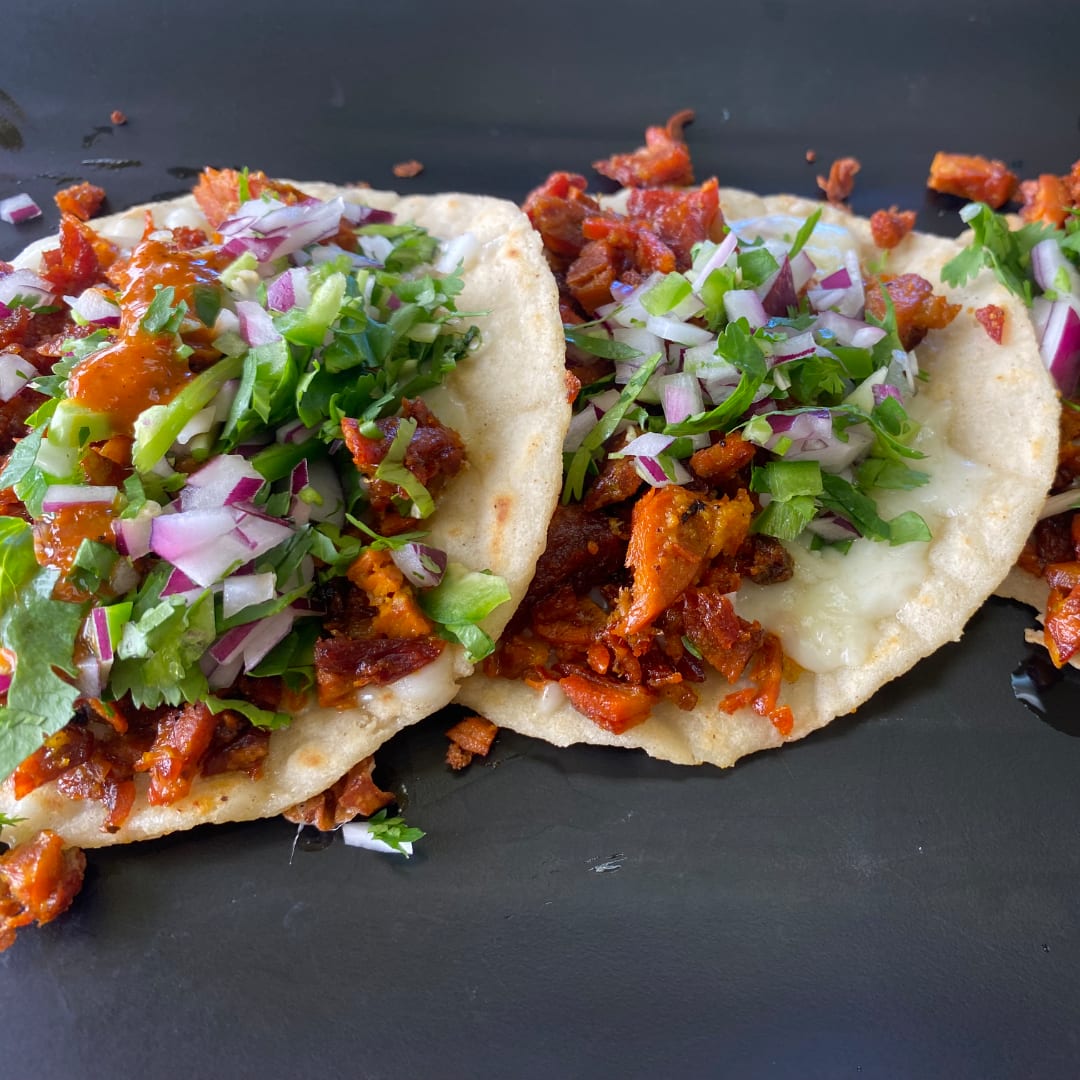 Two tacos topped with chopped onions, cilantro, and salsa on a dark plate