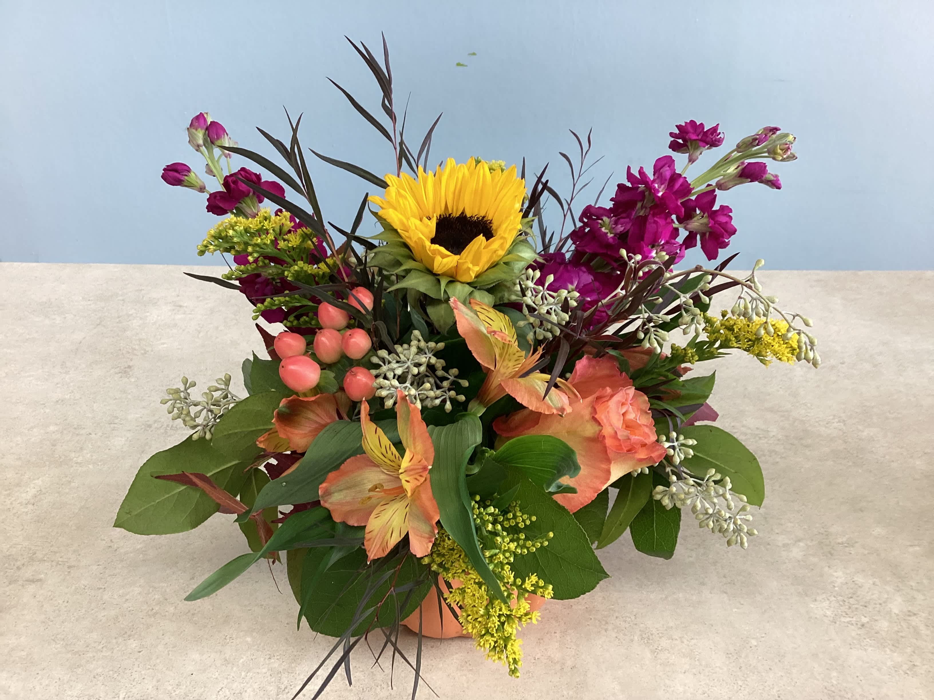 Mixed bouquet with a sunflower, pink blooms, and peach flowers in a low container