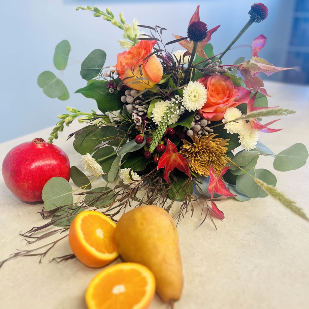 Autumn floral arrangement with orange roses and white mums beside fruit