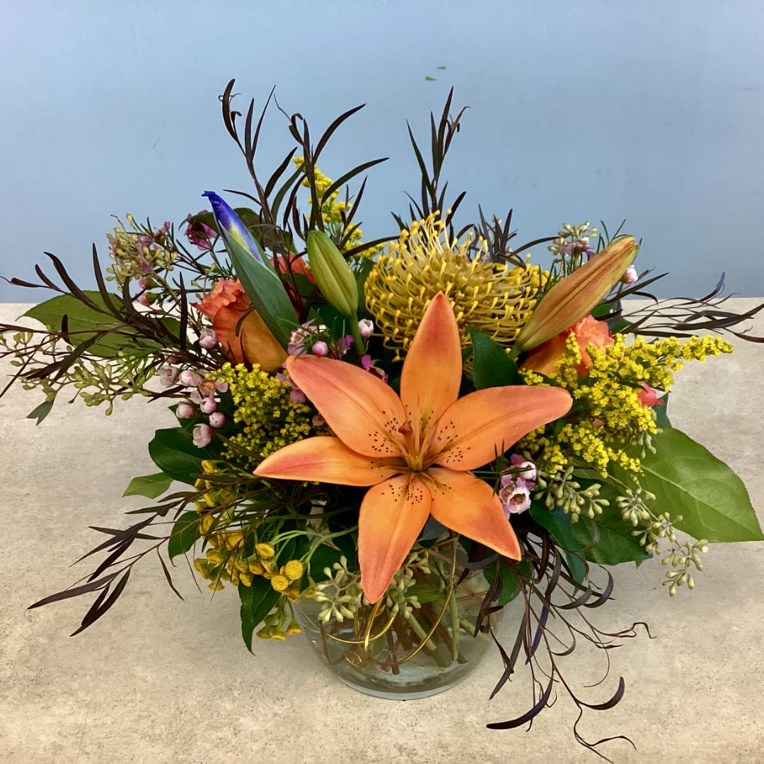 Orange lily bouquet in a clear glass vase with yellow and pink accents