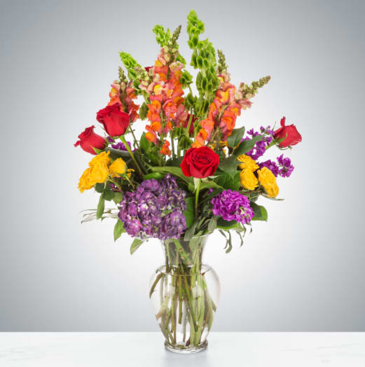 Floral Fantasy by BloomNation™ - A rich riot of colors, this mixed arrangement makes a big impression with all its different textures and premium flowers. Featuring red roses, peach snapdragons, bells of Ireland, purple hydrangea, and stock this arrangement makes a great anniversary or congrats gift.  Approximate Dimensions: 18"D x 25"H