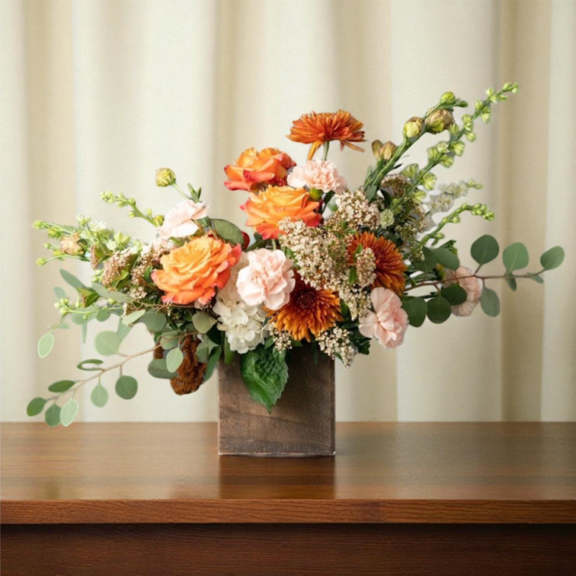 Orange and blush floral arrangement in a wooden vase