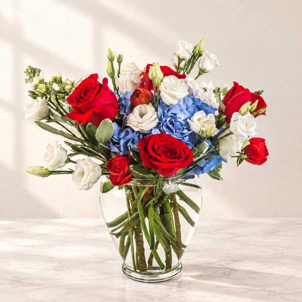 Red roses and white blooms arranged with blue hydrangeas in a clear glass vase.