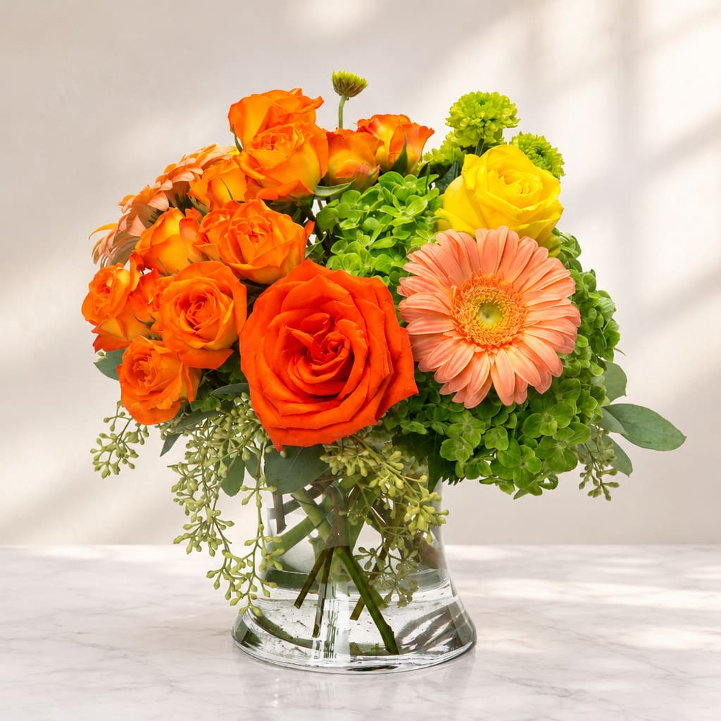 Orange and yellow roses with a peach gerbera daisy in a glass vase
