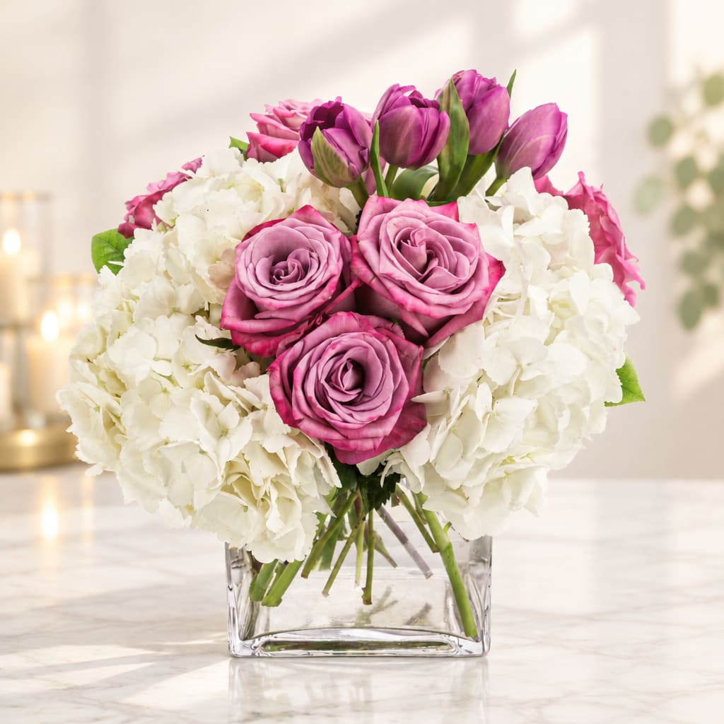 Pink roses and purple tulips in a clear square vase with white hydrangeas