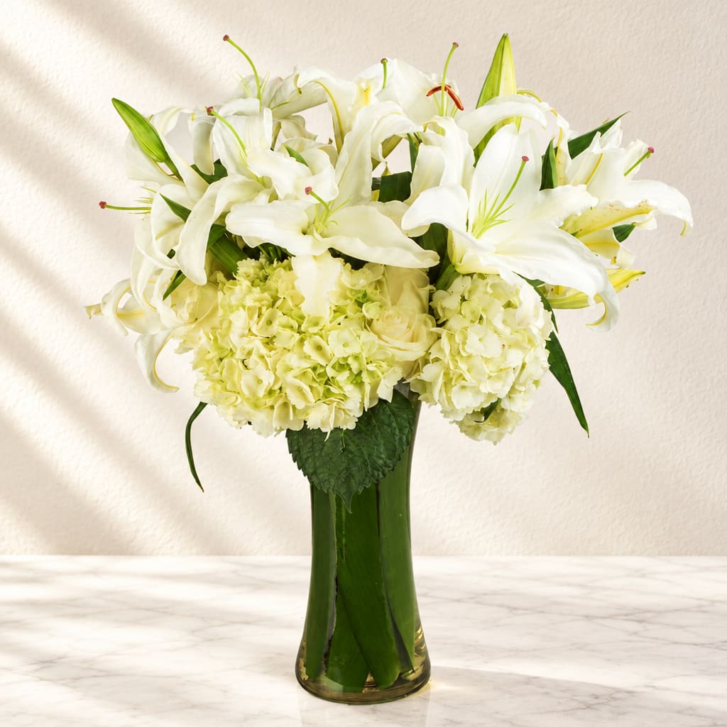 White lilies and pale hydrangeas arranged in a tall glass vase
