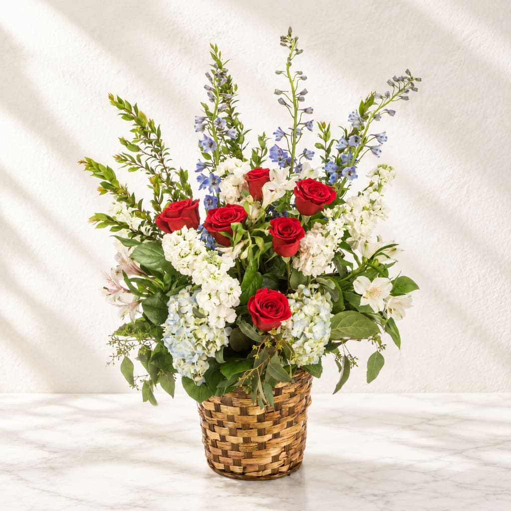 Basket arrangement of red roses, white blooms, and blue flowers