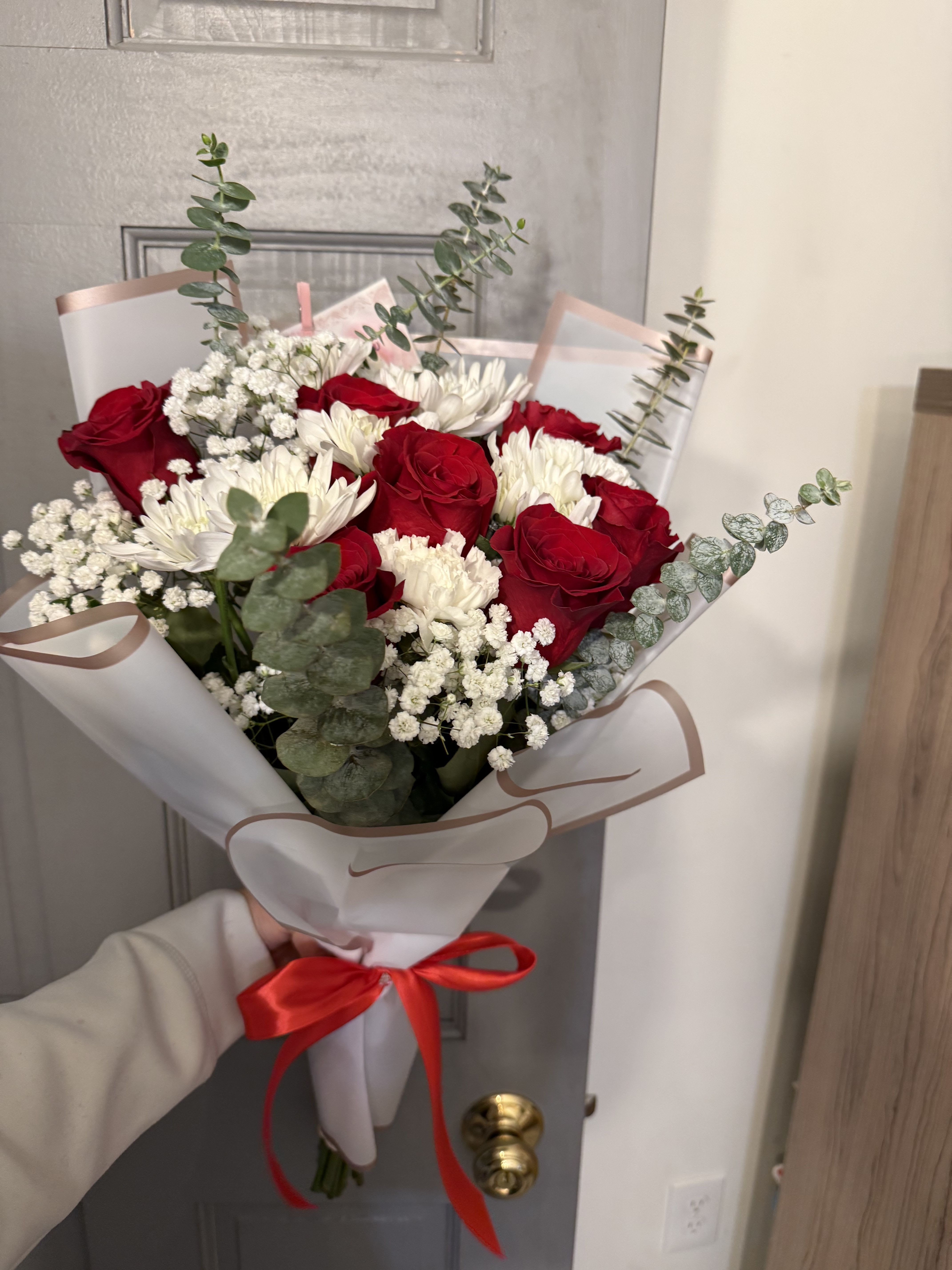Bouquet of red roses and white daisies wrapped in white paper with a red ribbon