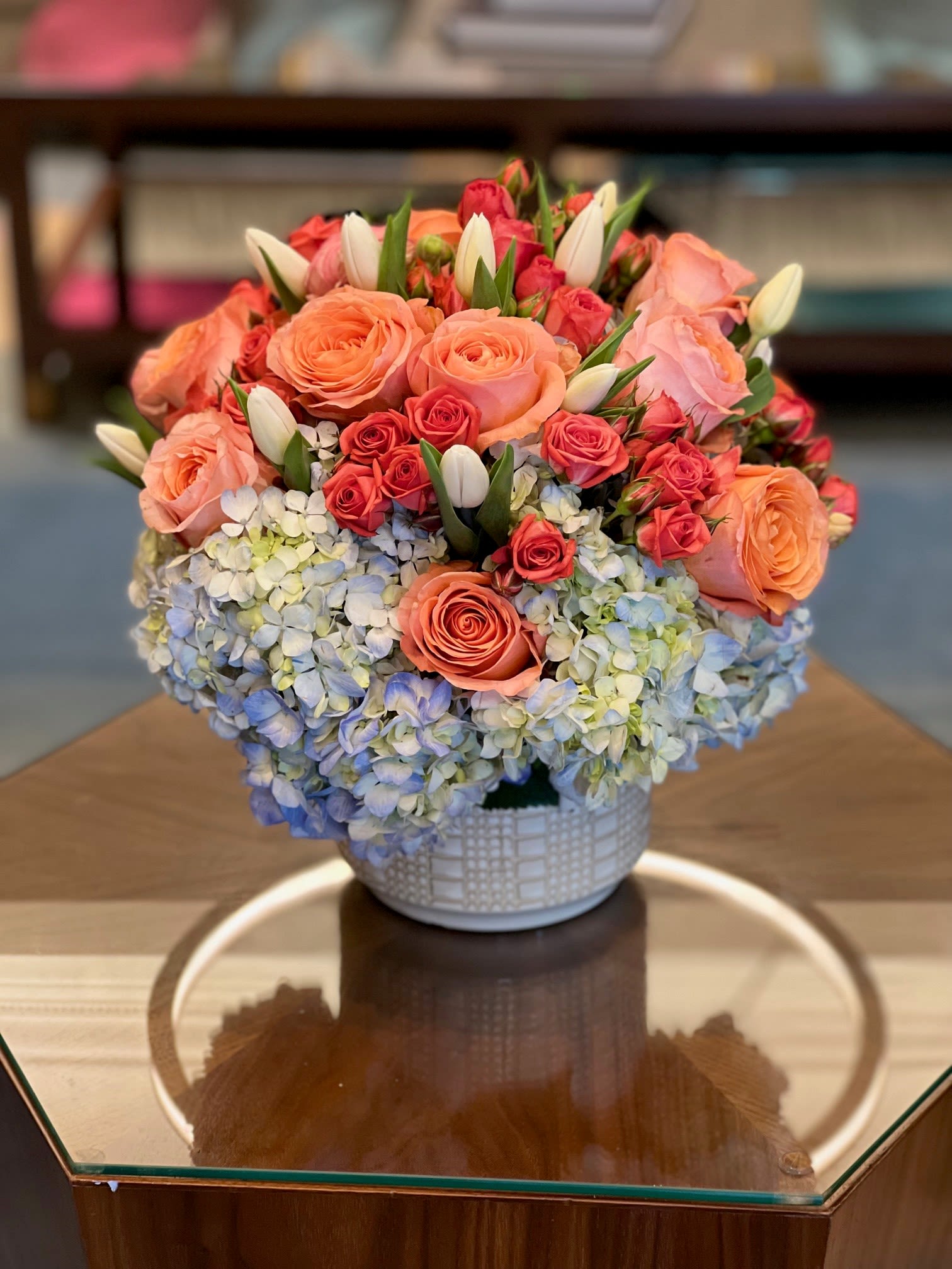 Peach and pink roses with blue hydrangeas in a white vase
