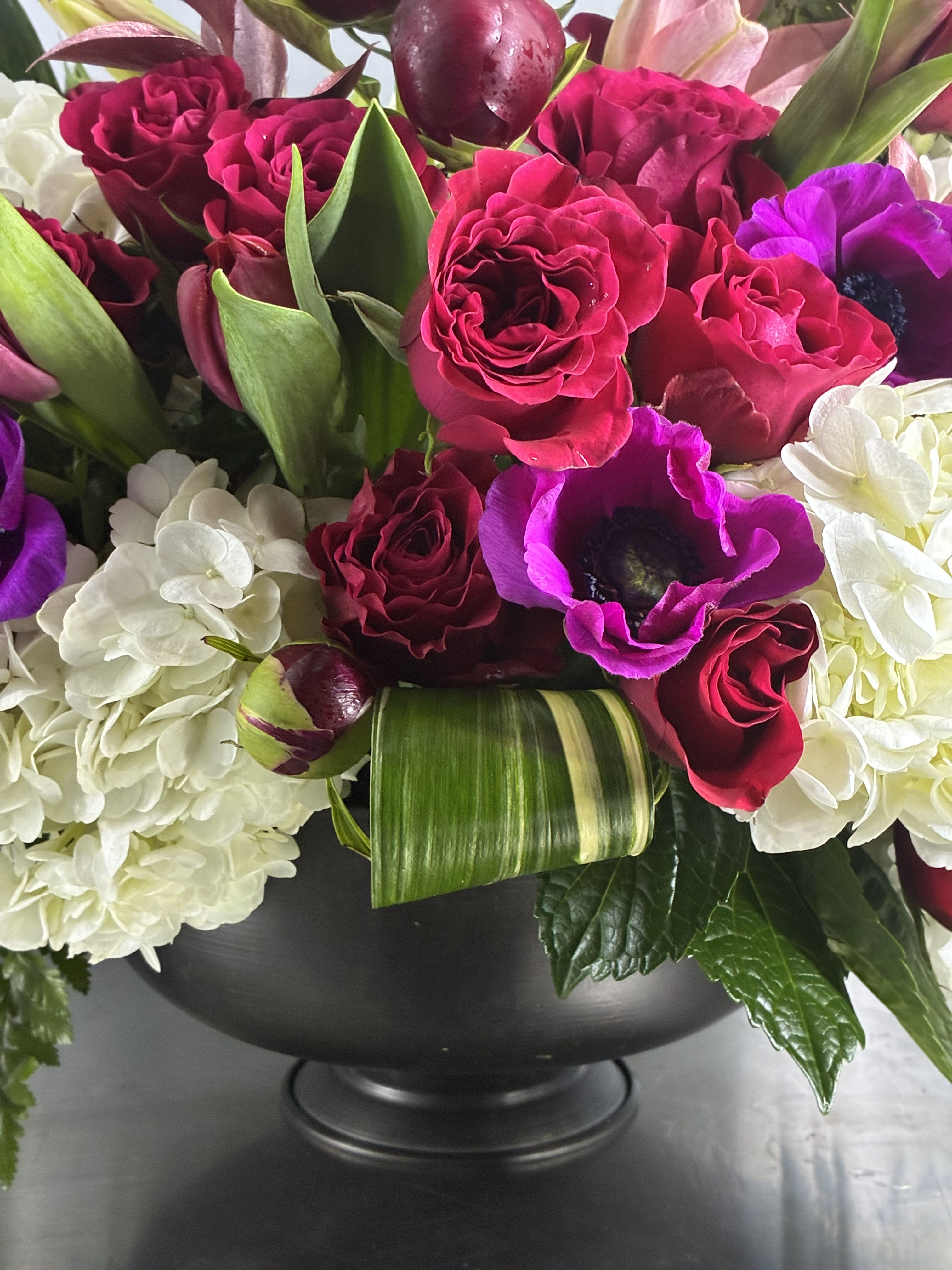 Bouquet of red roses, purple anemones, and white hydrangeas in a black vase
