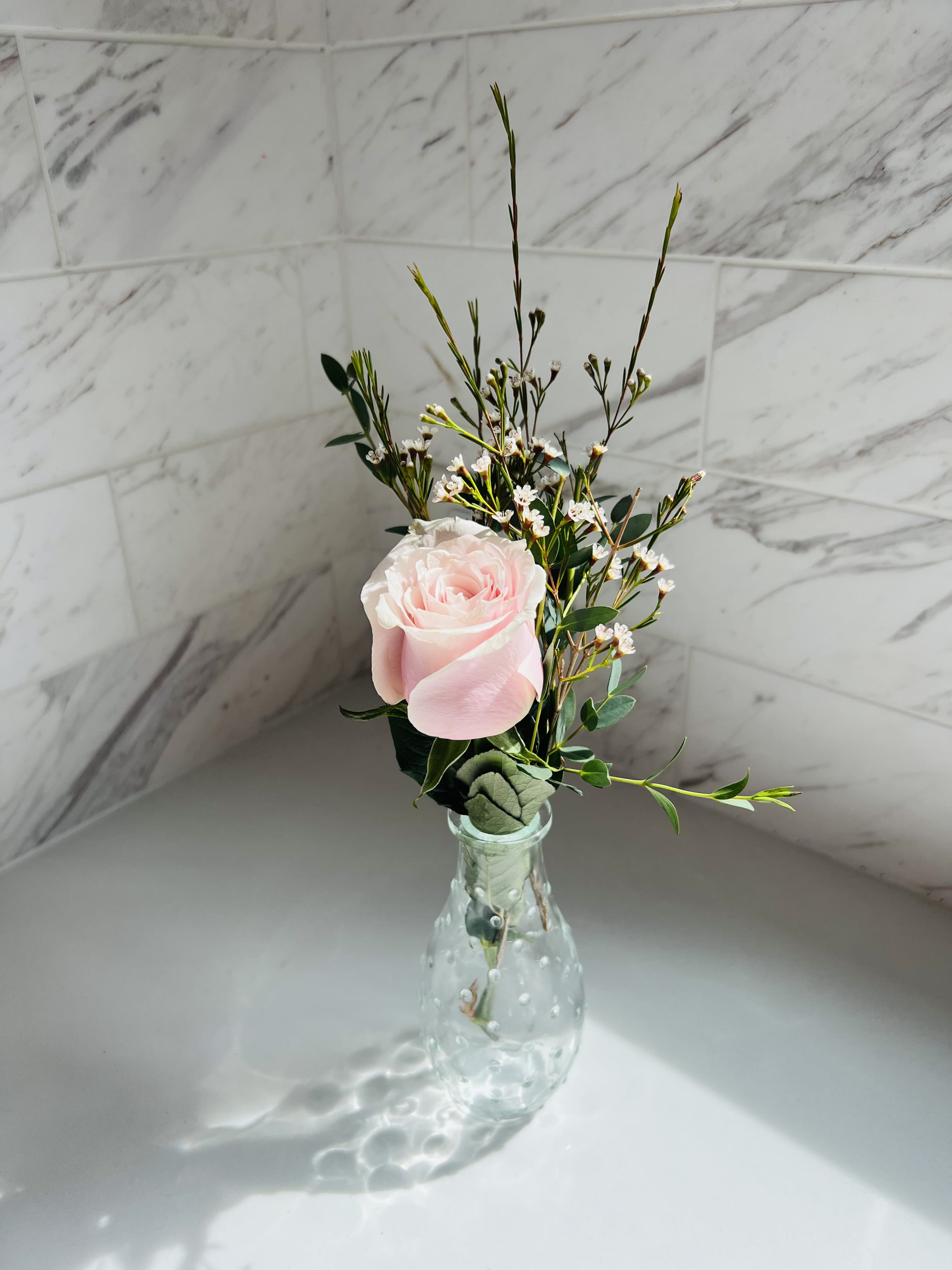 Single pale pink rose in a clear glass vase with airy filler flowers