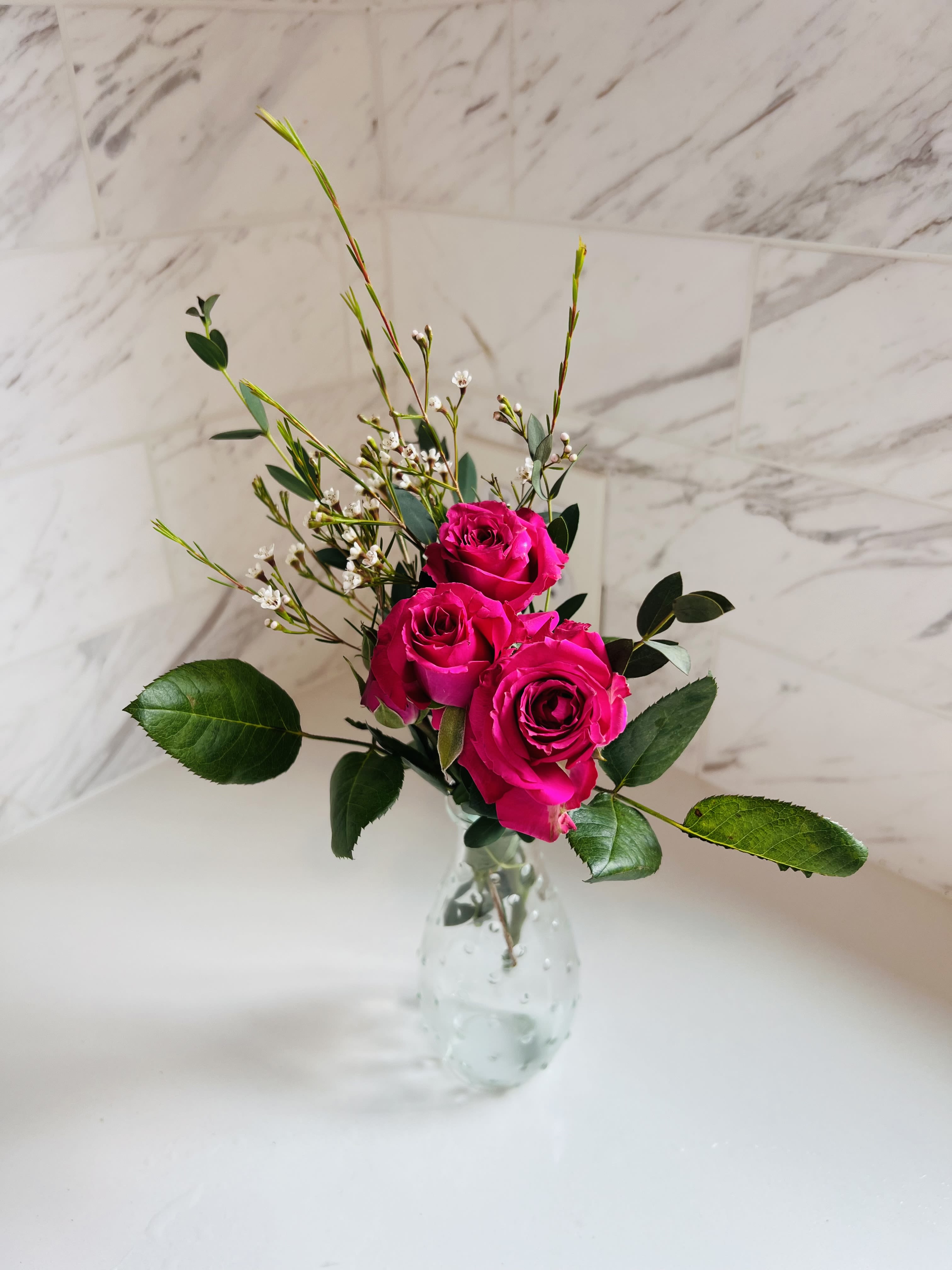 Three hot pink roses in a clear glass vase with small white filler flowers
