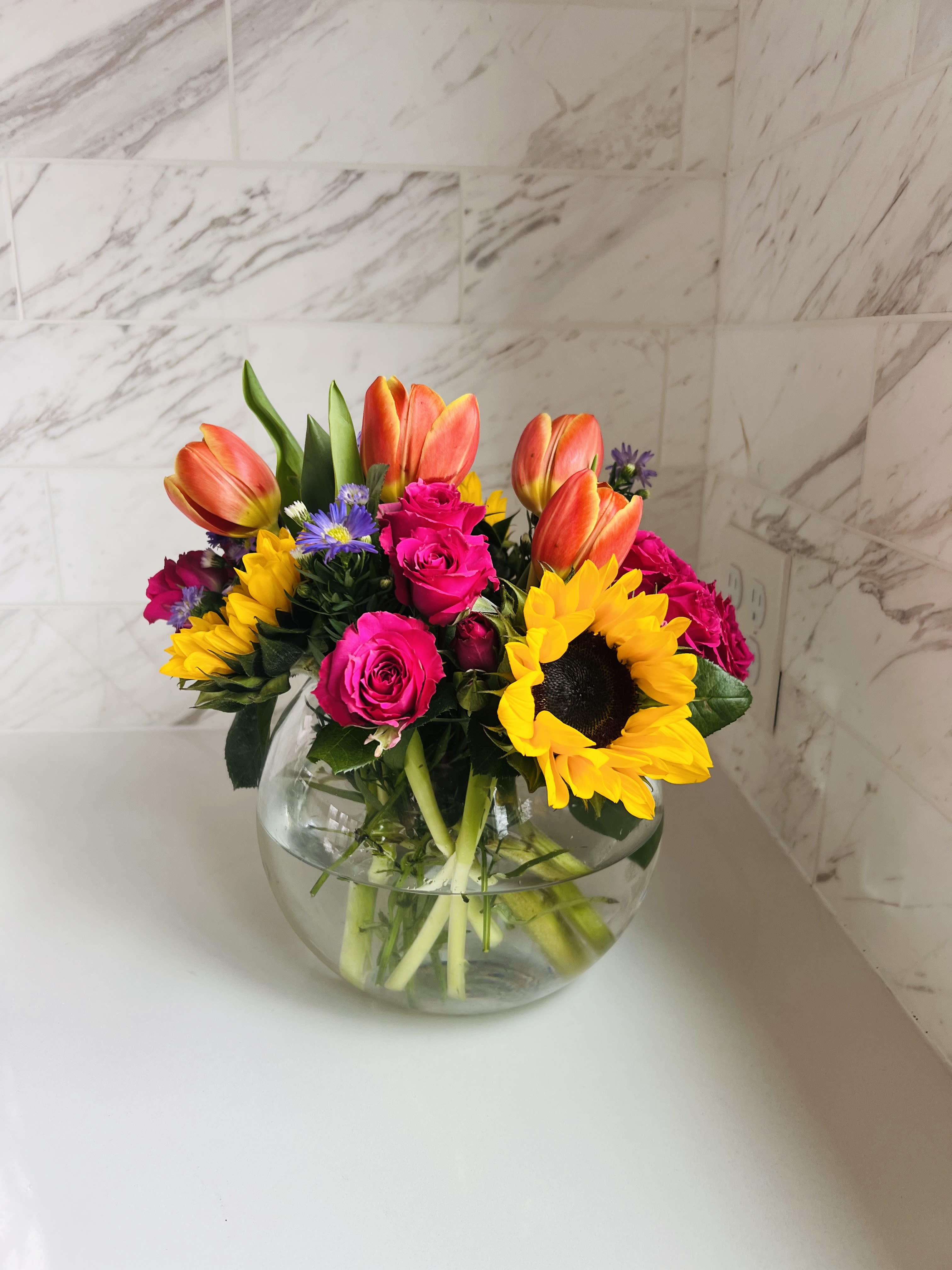Bouquet of tulips, roses, and sunflowers in a round glass vase