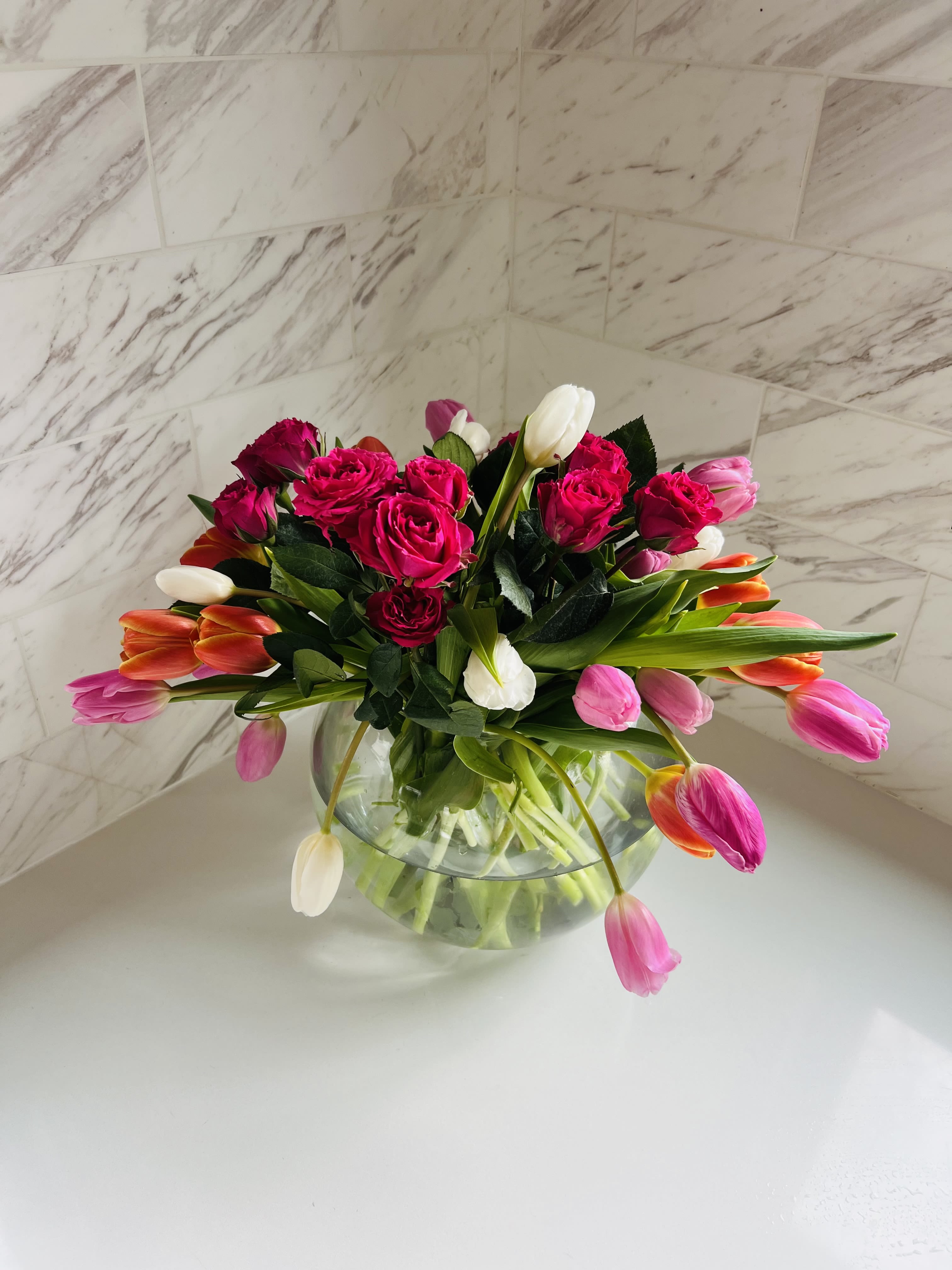 Pink roses and tulips arranged in a clear glass bowl vase