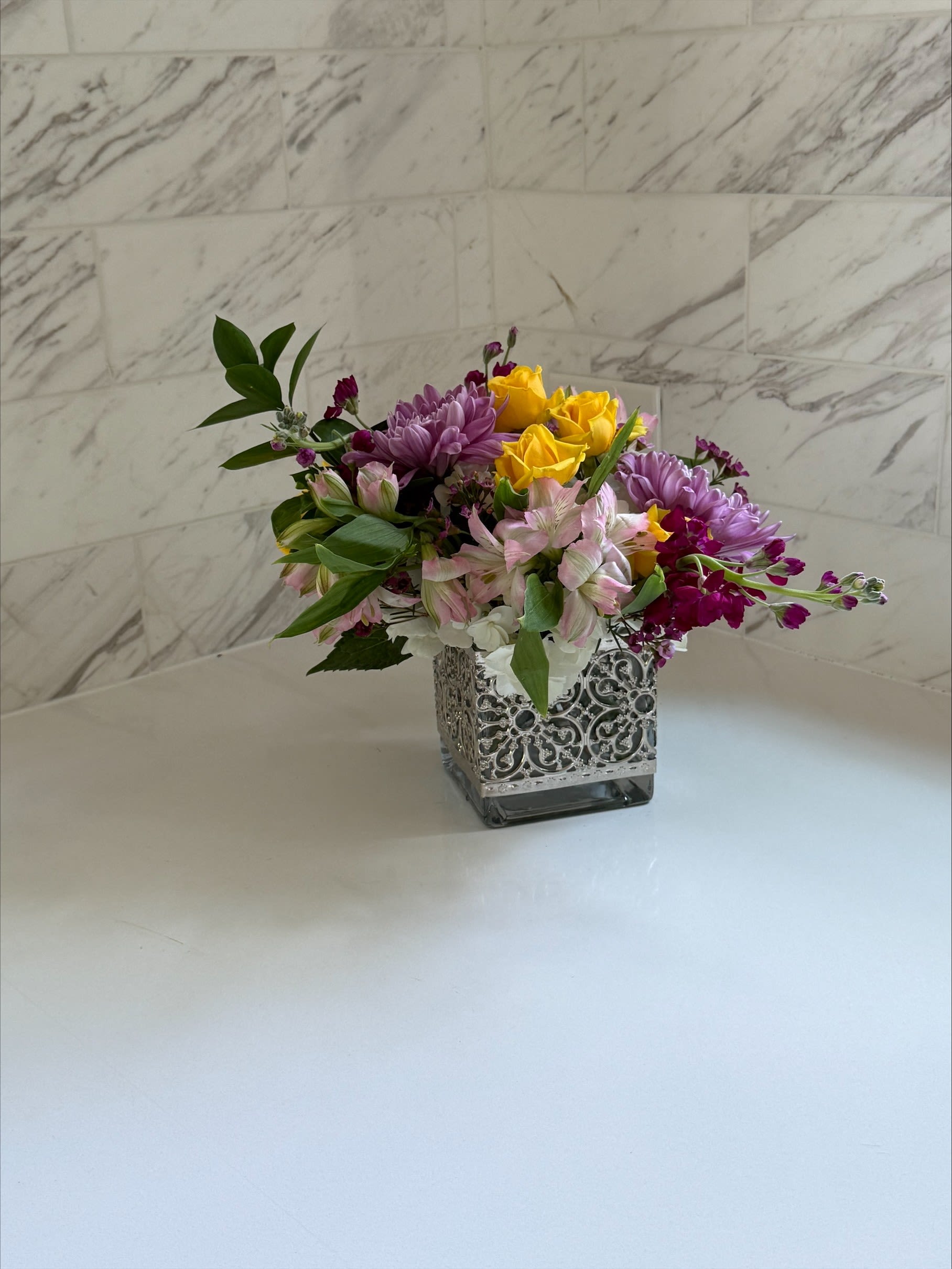 Mixed bouquet in a decorative square vase with yellow, purple, and pink flowers
