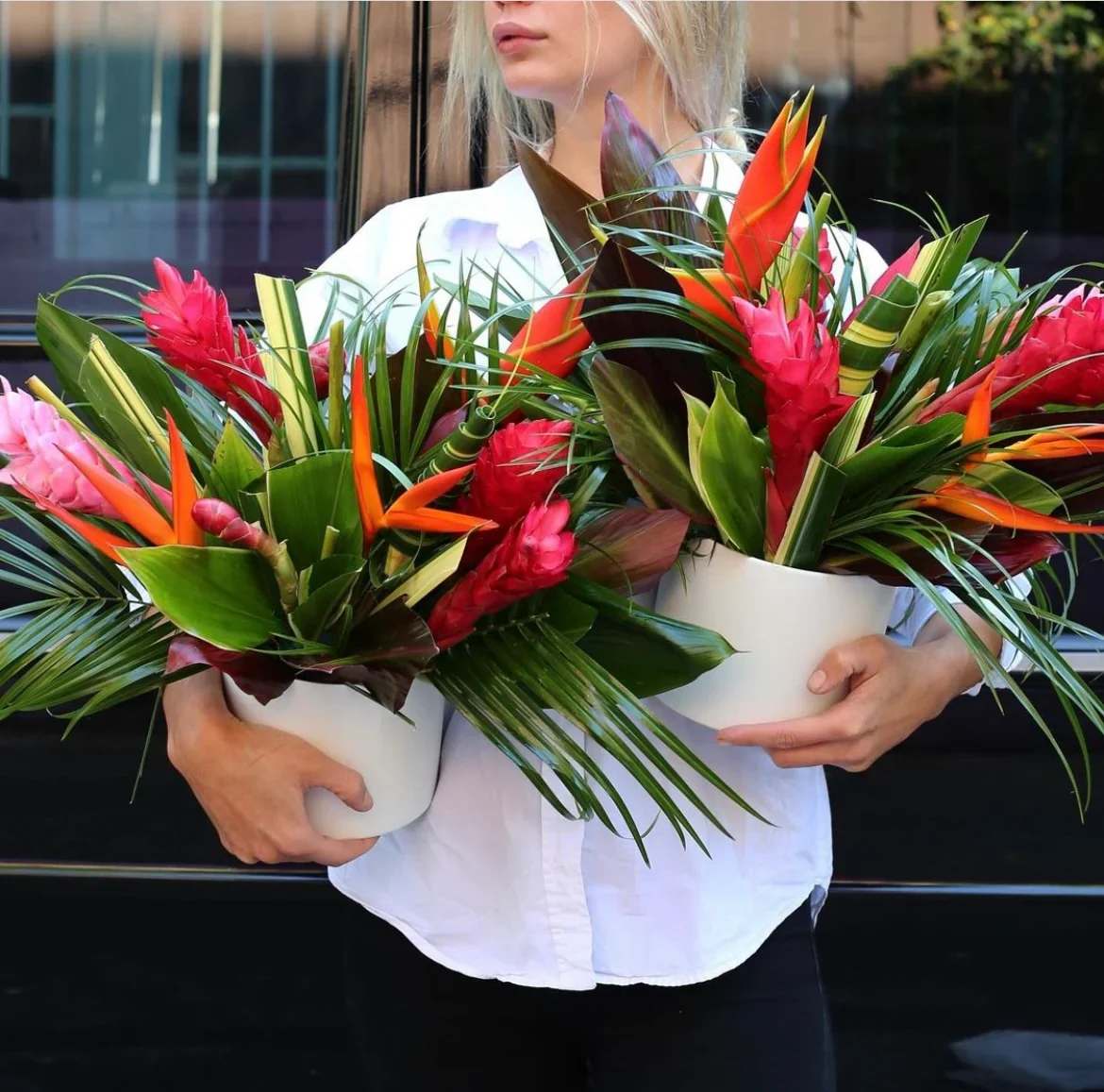 Two tropical flower arrangements in white pots held by a person