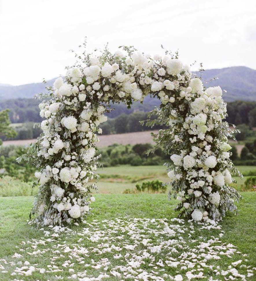 White floral arch outdoors with petals scattered on grass