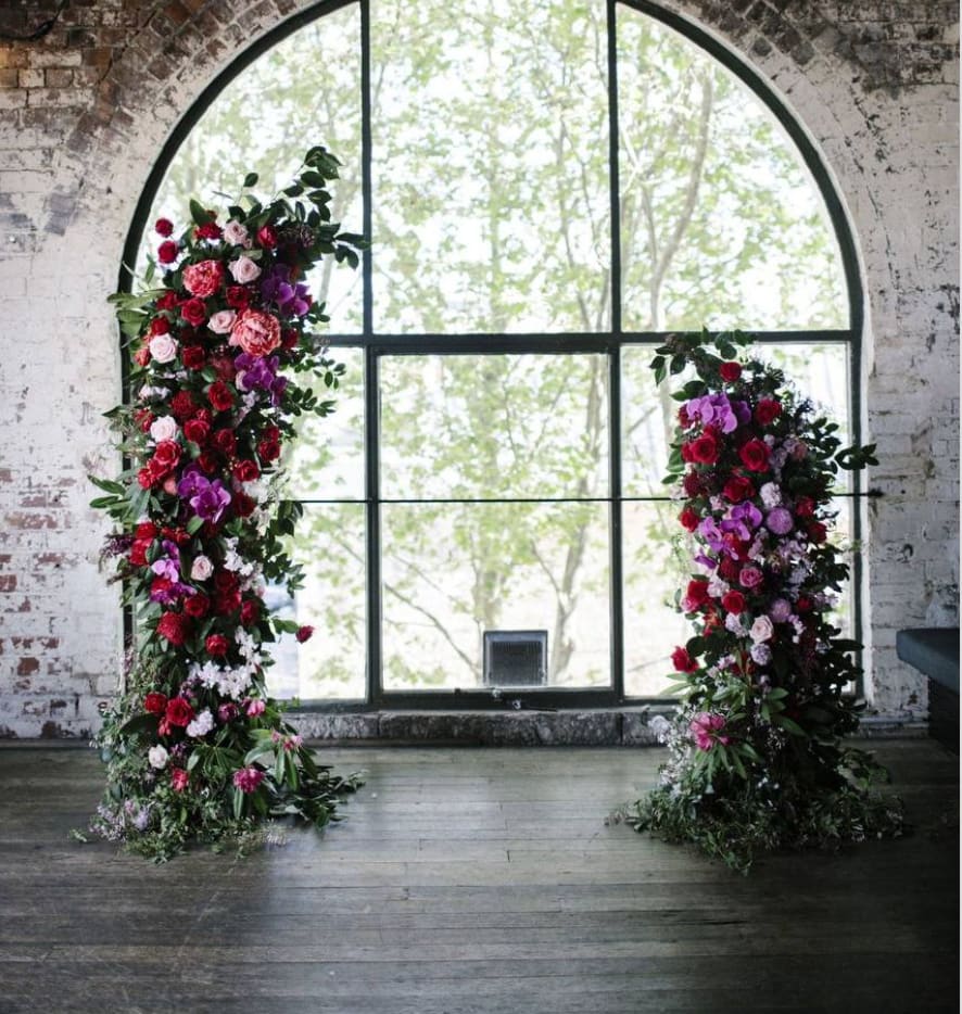Two tall floral pillars with red, pink, and purple blooms by a large window