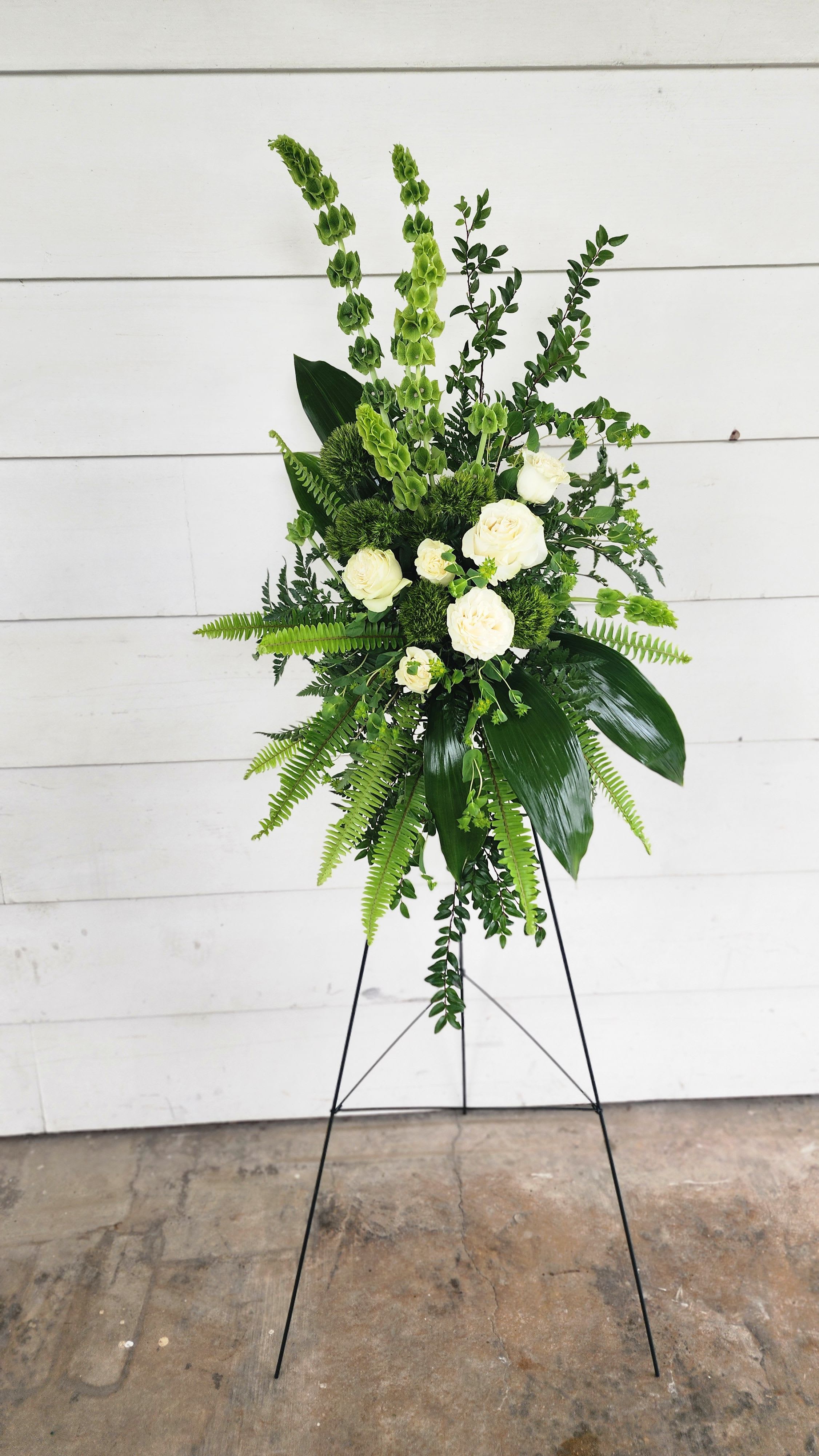 Evergreen Serenity - Evergreen Serenity is a graceful and timeless standing spray that embodies peace, renewal, and everlasting remembrance. Lush green accents weave through a delicate arrangement of white lilies, roses, and chrysanthemums, symbolizing purity and eternal love. Soft ferns and eucalyptus add a natural elegance, creating a soothing tribute that offers comfort and solace. Perfect for honoring a loved one, Evergreen Serenity stands as a beautiful expression of sympathy, hope, and enduring memory.