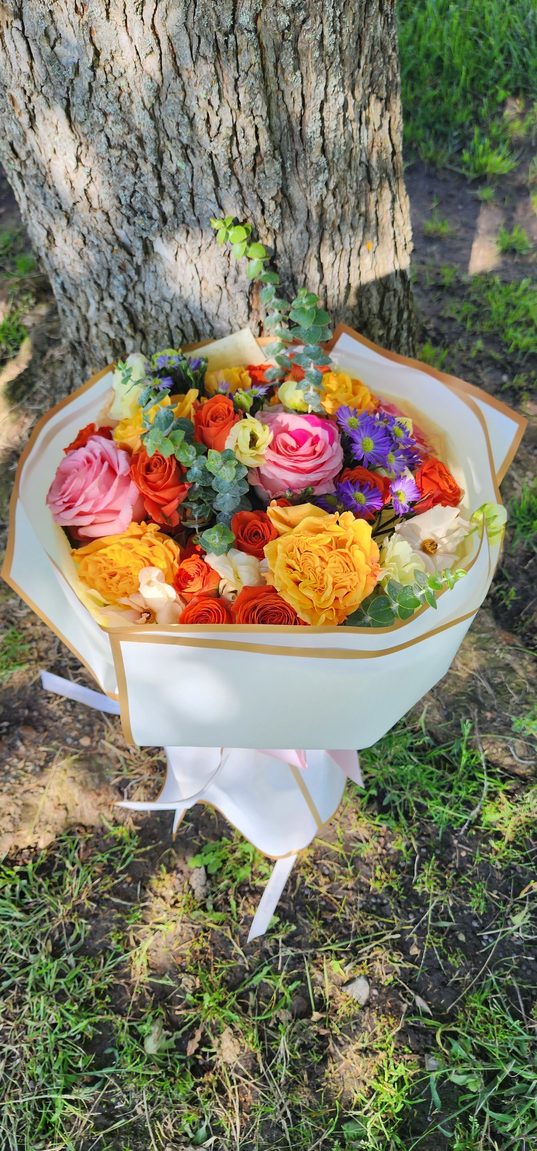 Bouquet of pink, yellow, orange, and purple flowers wrapped in white paper