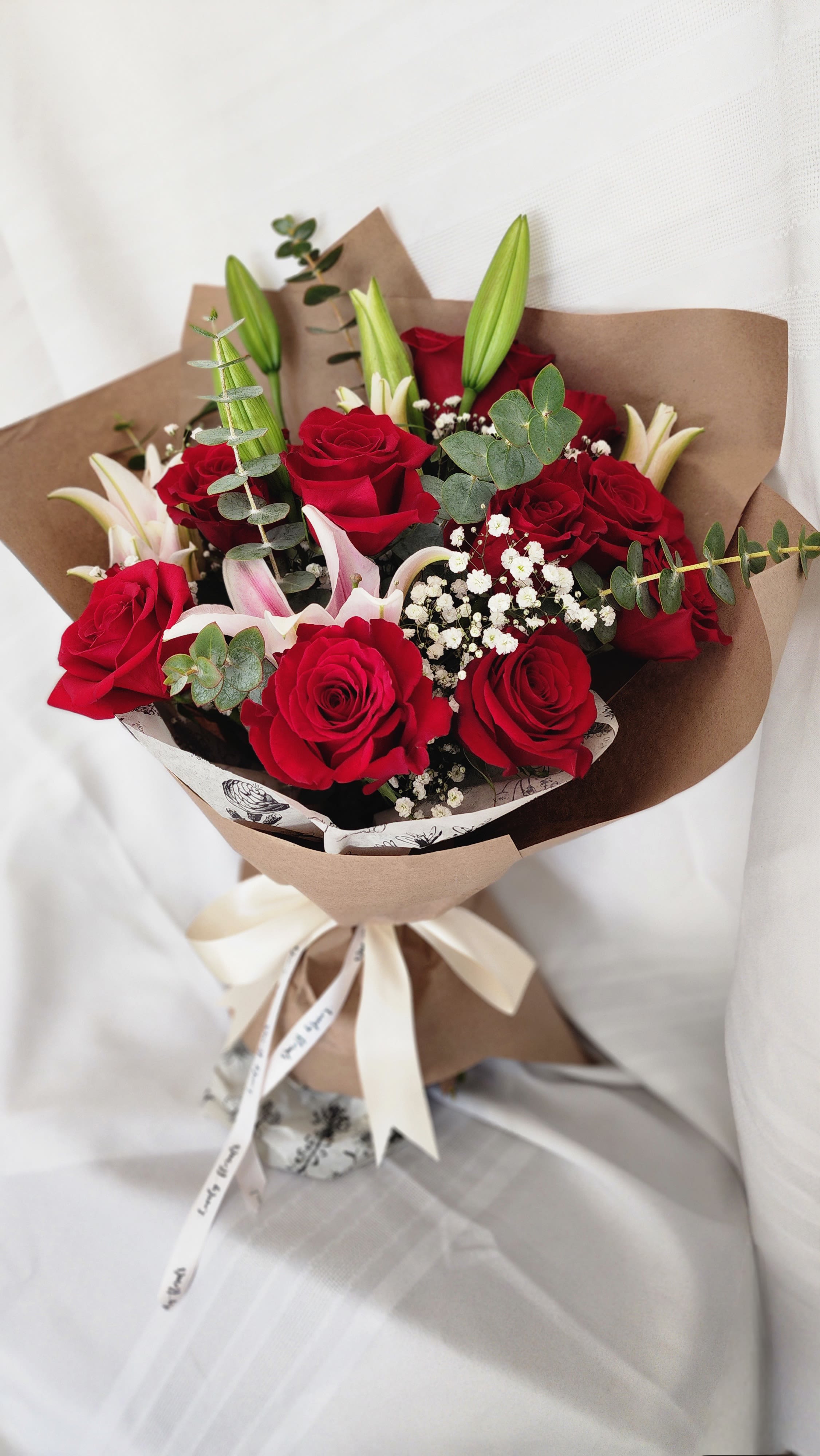 Dozen Red Roses -Paper  Wrapped  - This is our classic hand Wrapped Bouquet. Dozen Red Roses with stargazer lilies and some baby breath wrapped in a paper cover.