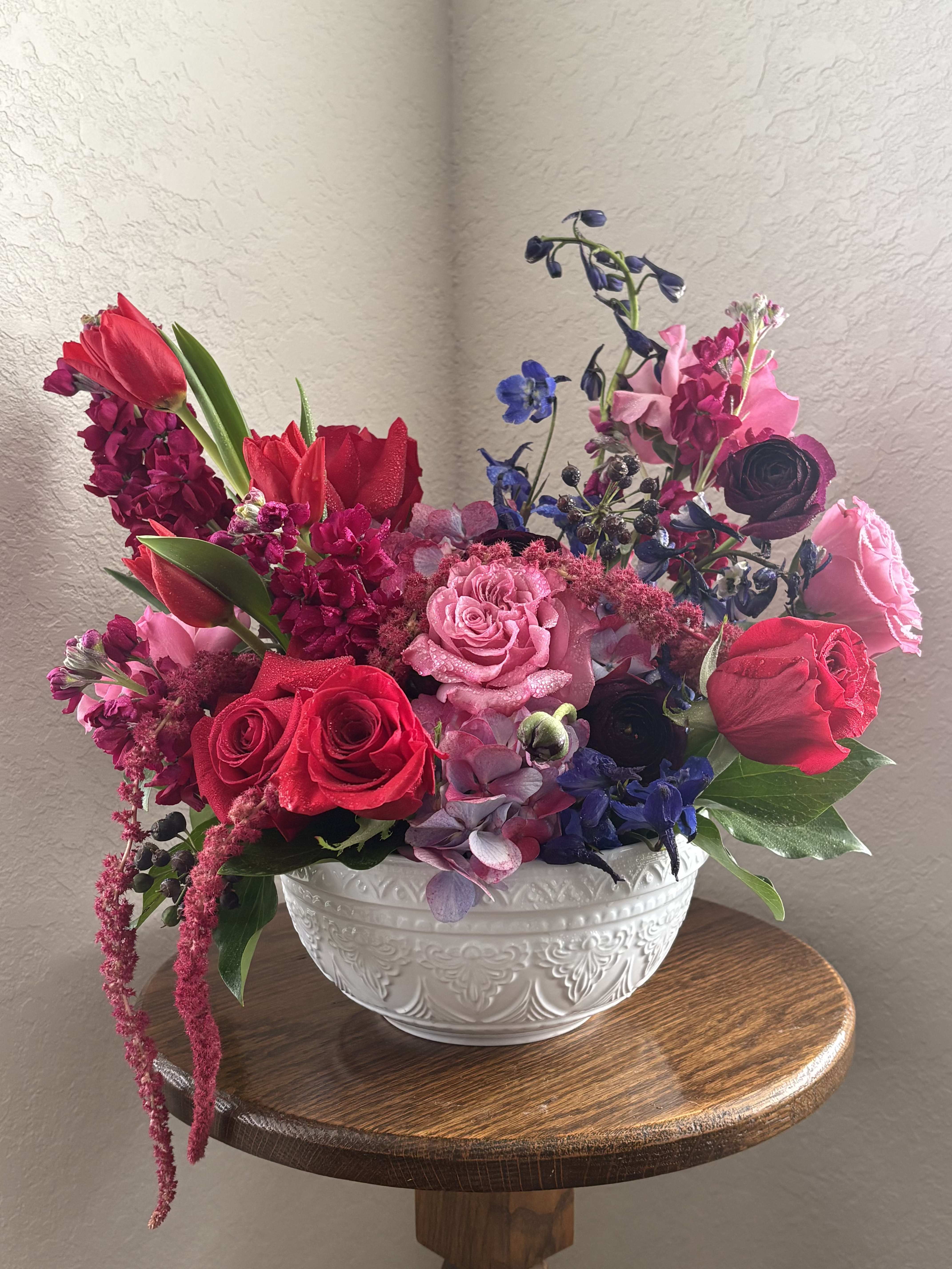 Mixed bouquet of red, pink, and blue flowers in a white bowl vase