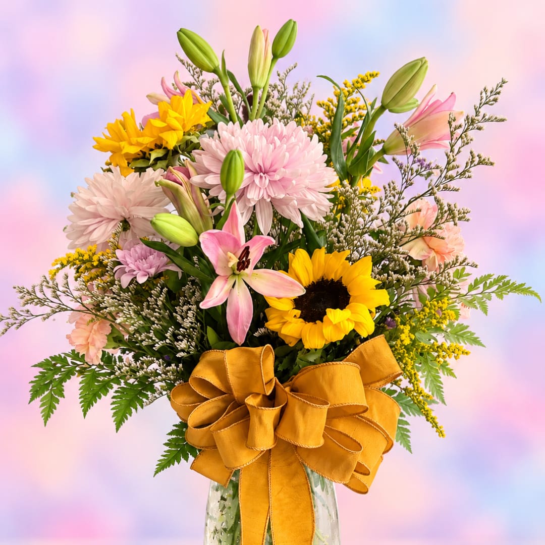 Bouquet of pink lilies, sunflowers, and chrysanthemums in a glass vase with a gold ribbon.