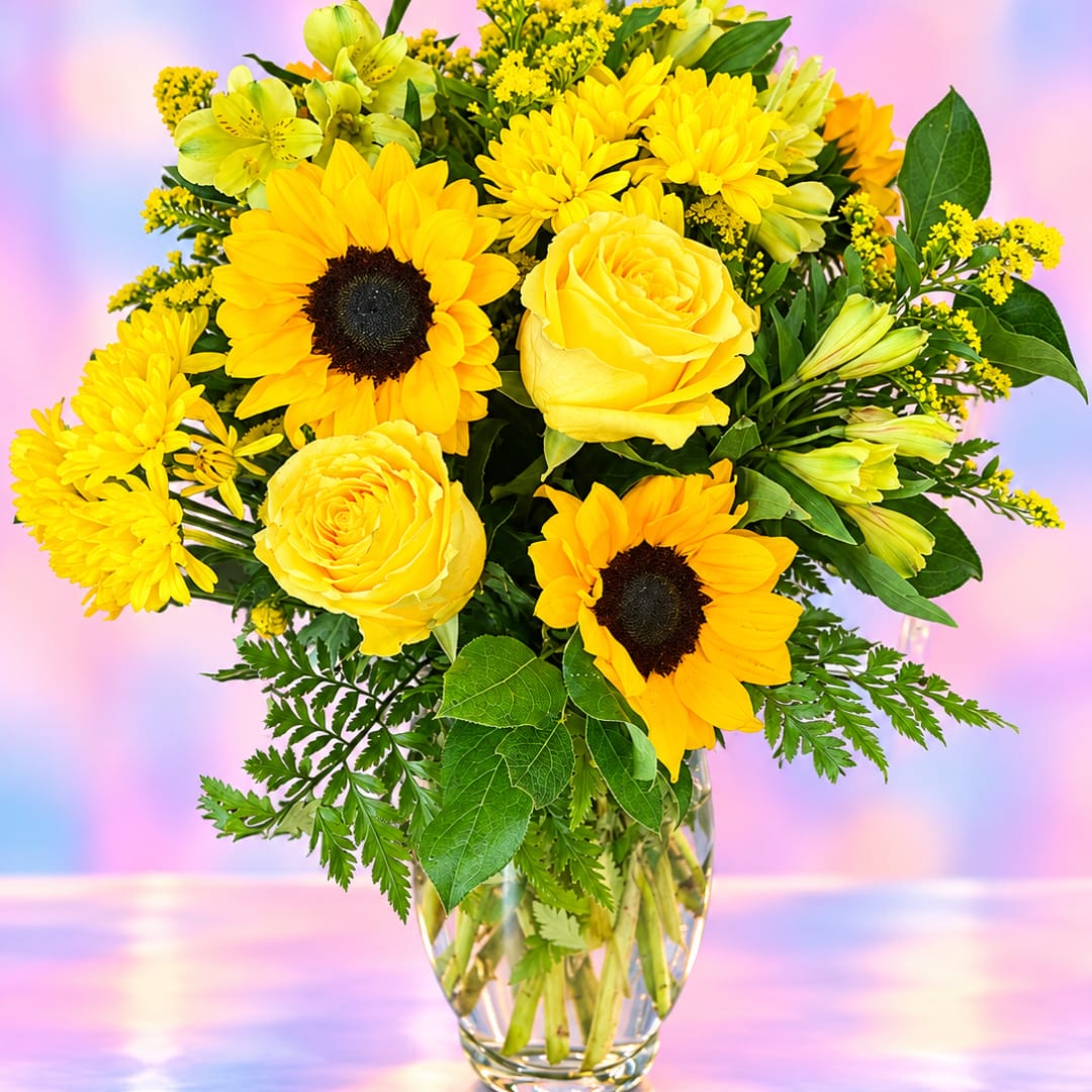 Yellow roses, sunflowers, and daisies in a clear glass vase