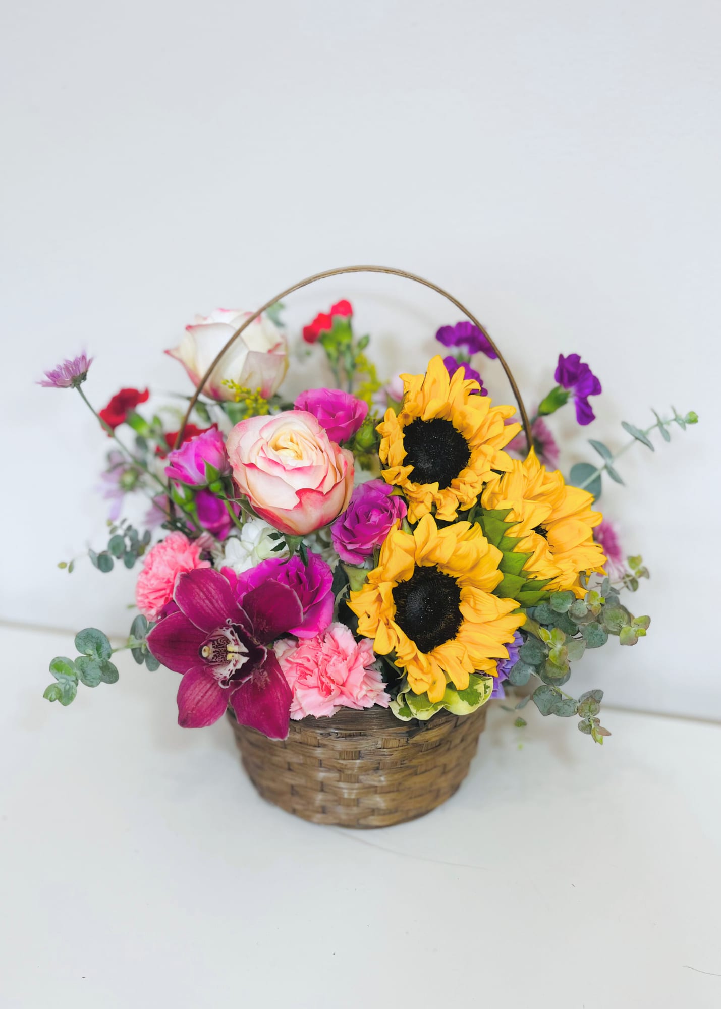 Colorful basket arrangement with sunflowers, roses, carnations, and an orchid in a woven basket