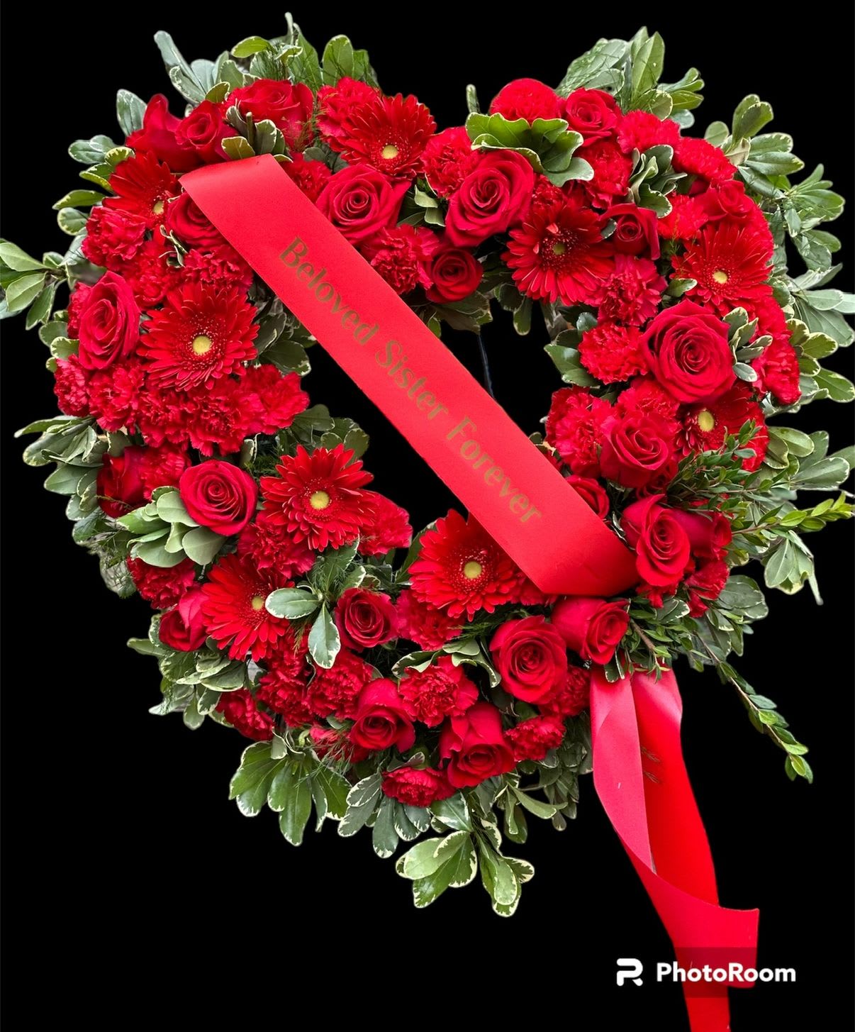 Ruby Remembrance Heart: - This striking arrangement is a heart-shaped standing floral tribute, crafted specifically for memorial services or funerals. It features a lush, vibrant display of radiant red blooms, including roses and carnations, often associated with deep love, respect, and admiration in funeral arrangements. The arrangement is meticulously designed in the classic heart shape, a powerful and universally recognized symbol of love, affection, and heartbreak, conveying profound emotion and remembrance for the departed