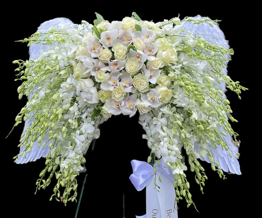 Heavenly Ascent - This exquisite floral arrangement, designed in the ethereal shape of angel wings, embodies a profound sense of peace, purity, and remembrance. Crafted predominantly with a blend of pristine white and soft cream blooms, it features an opulent central cluster of delicate roses and elegant orchids, and Dendrobium orchids, that gracefully cascades downwards.