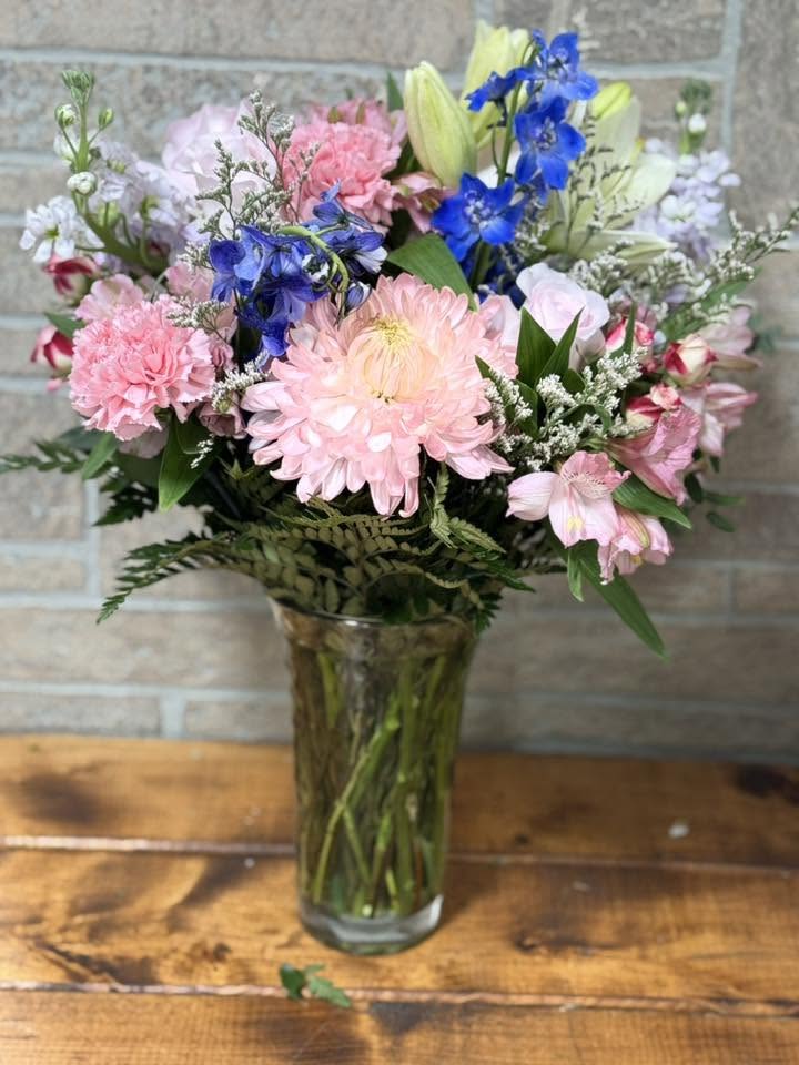 Delphinium Garden - Bring the beauty of a blooming garden indoors with Delphinium Garden, a graceful floral arrangement showcasing stunning delphinium blooms among a gathering of fresh seasonal flowers and lush greenery. Known for their tall, elegant stems and vibrant blue hues, delphiniums symbolize dignity, positivity, and an open heart, making this arrangement a meaningful gift for any occasion.