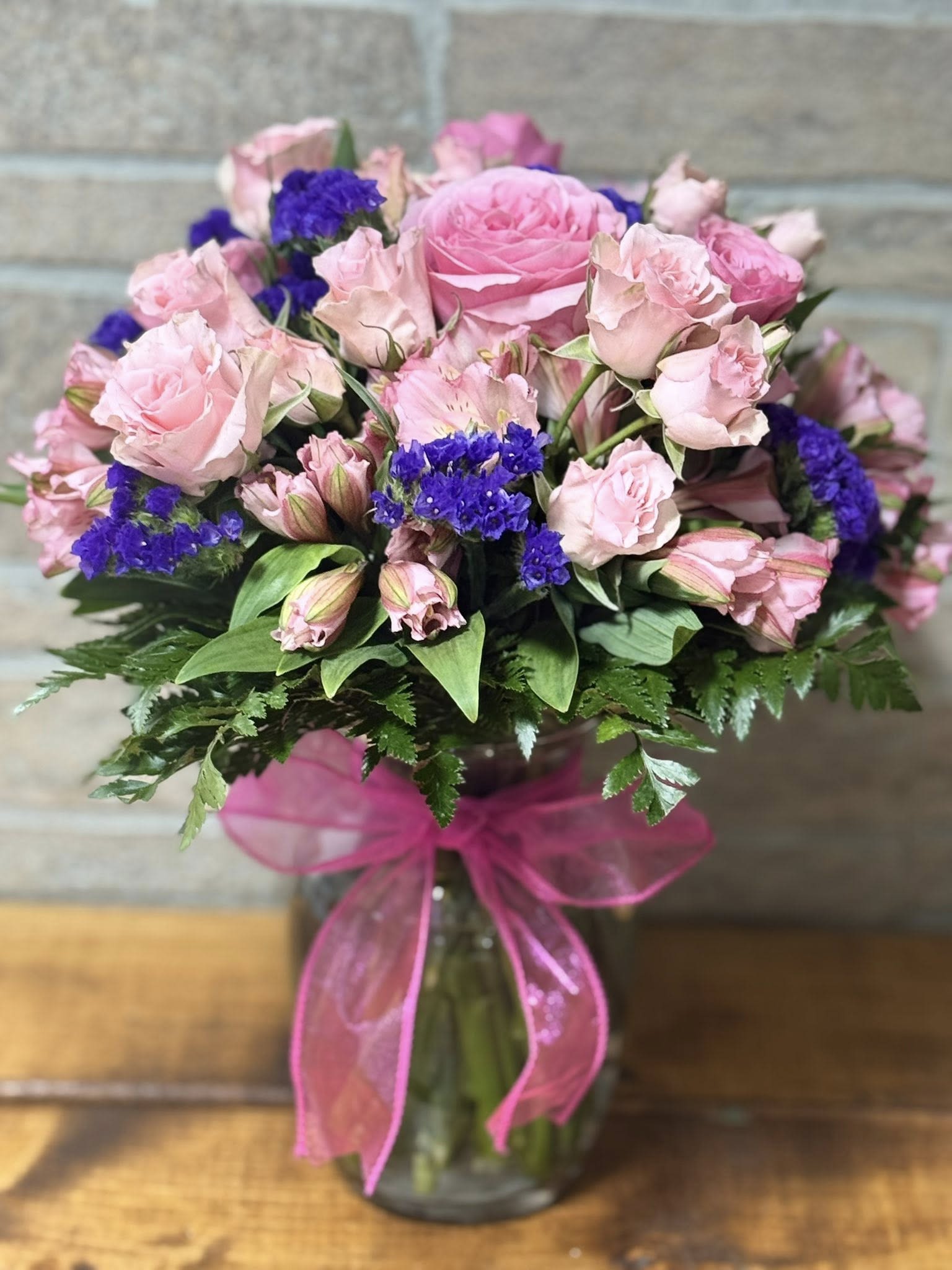 Blushing Amethyst Garden - The Blushing Amethyst Garden is a lush floral arrangement featuring a romantic blend of soft pink and rich purple blooms designed to create a striking yet elegant display. This arrangement showcases premium roses, seasonal pink florals, and deep purple accents, beautifully arranged with fresh greenery for natural texture and depth. Perfect for birthdays, anniversaries, sympathy tributes, or everyday gifting, this design brings a graceful balance of softness and bold color.