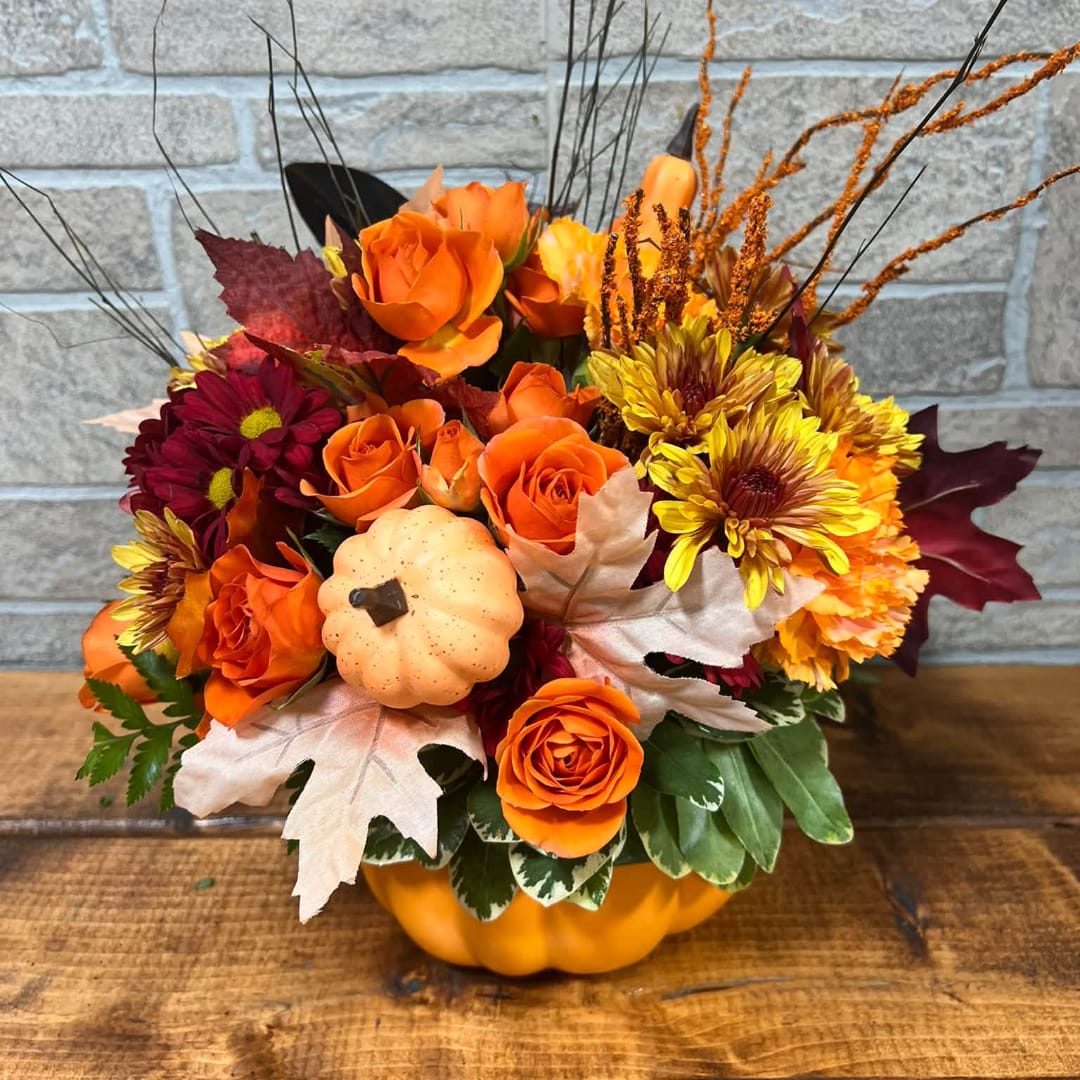 Orange roses and mums arranged in a pumpkin container with autumn leaves