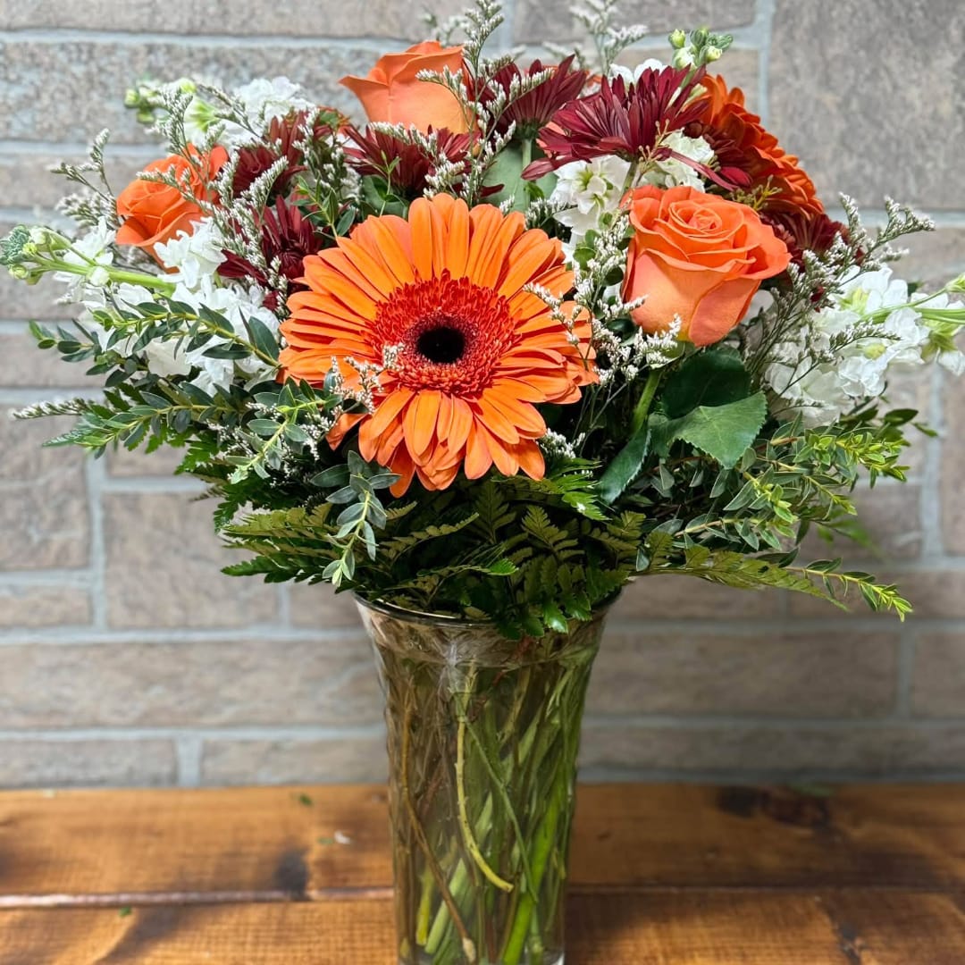 Orange gerbera daisies and roses in a clear glass vase
