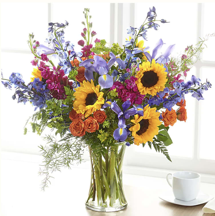 Mixed bouquet of sunflowers, irises, and orange roses in a glass vase