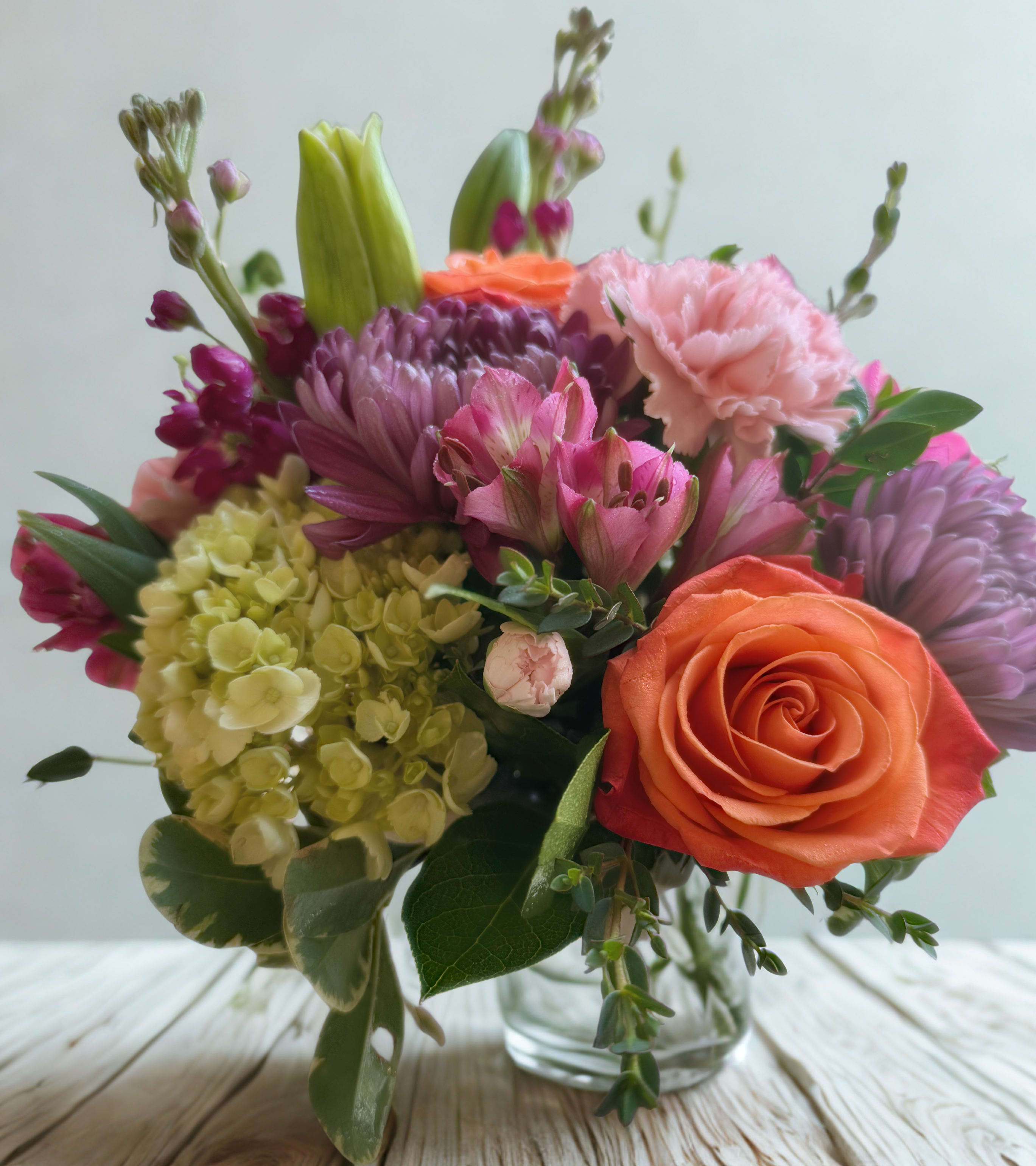 Mixed bouquet with roses, carnations, hydrangea, and lilies in a glass vase