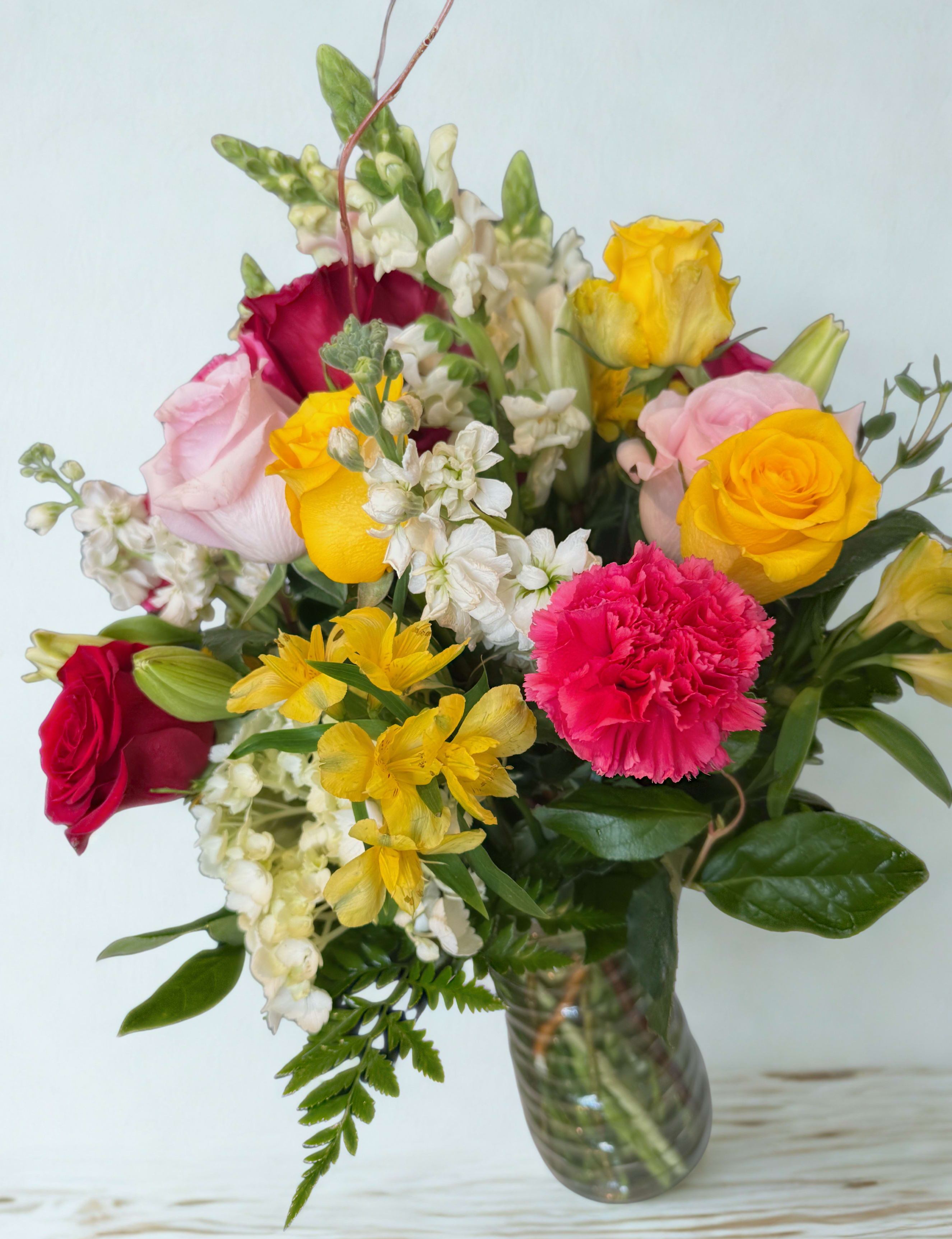 Mixed bouquet of roses, carnations, and white filler flowers in a glass vase