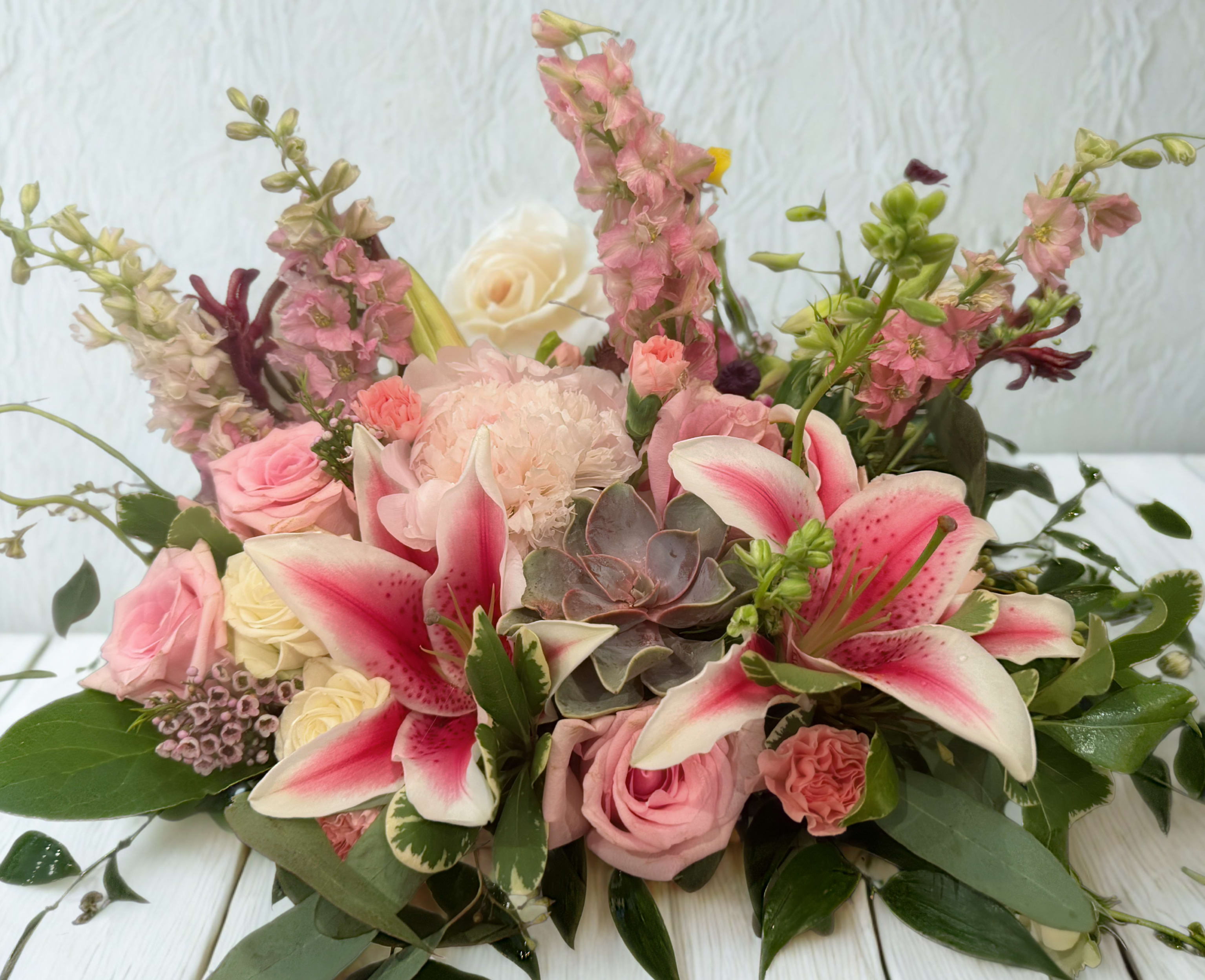 Pink lilies and roses arranged with a succulent in a low bouquet