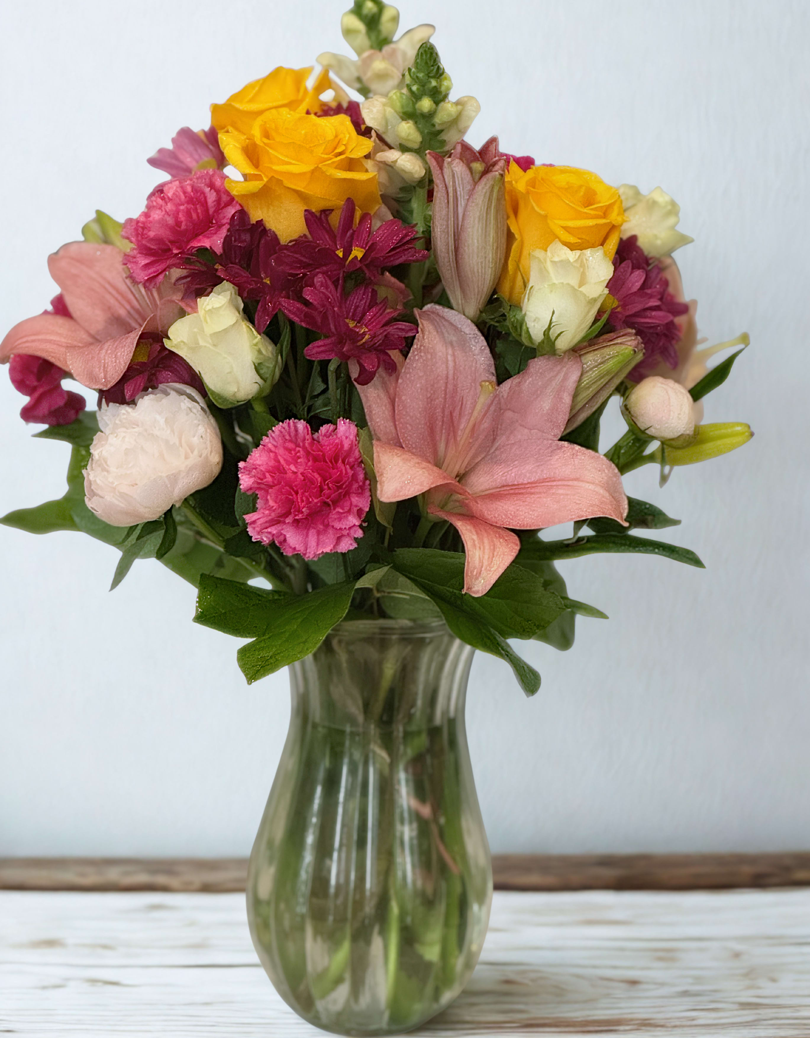 Mixed bouquet of pink, yellow, and white flowers in a glass vase