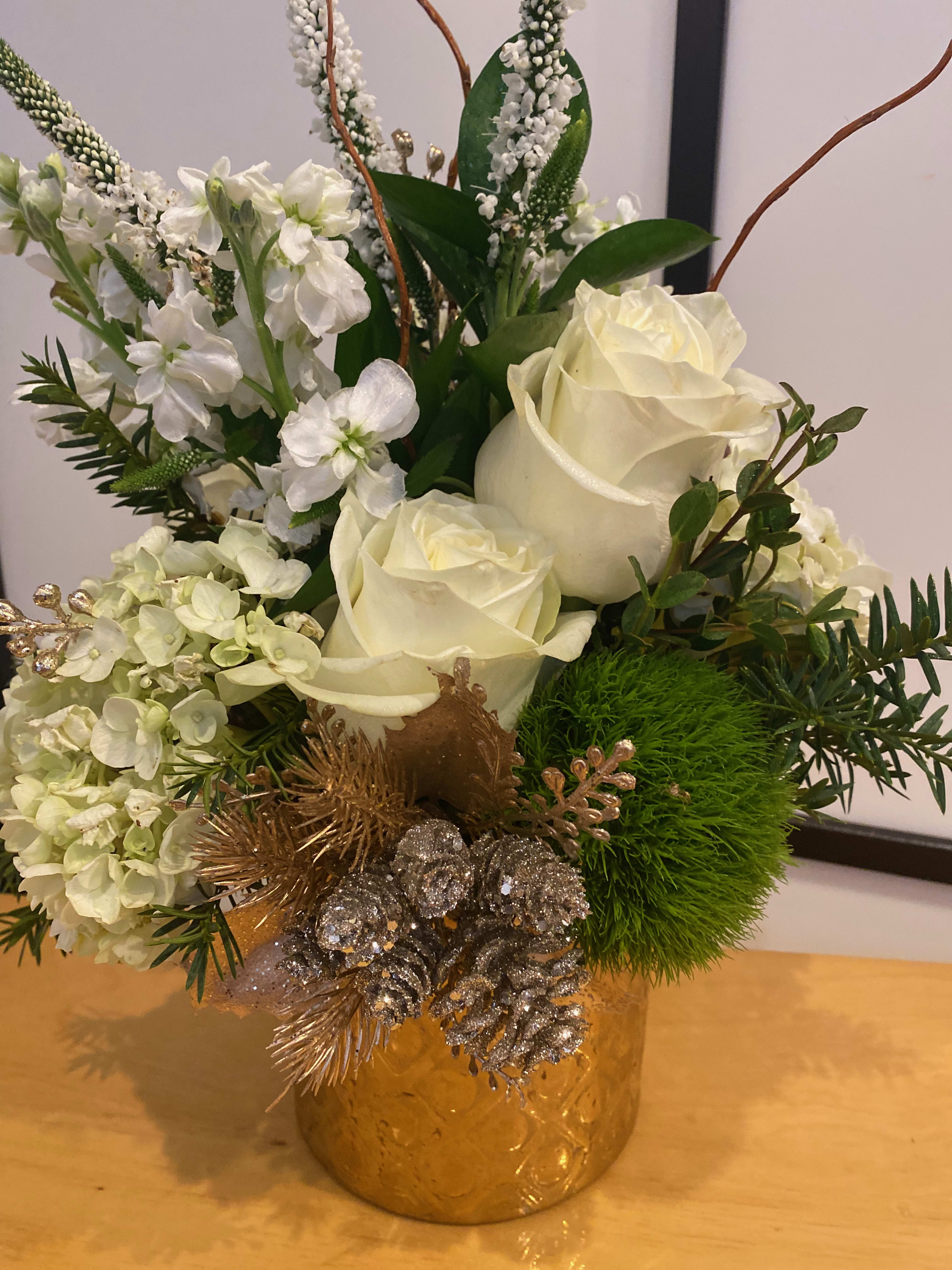 White roses and hydrangeas in a gold vase with silver pinecones