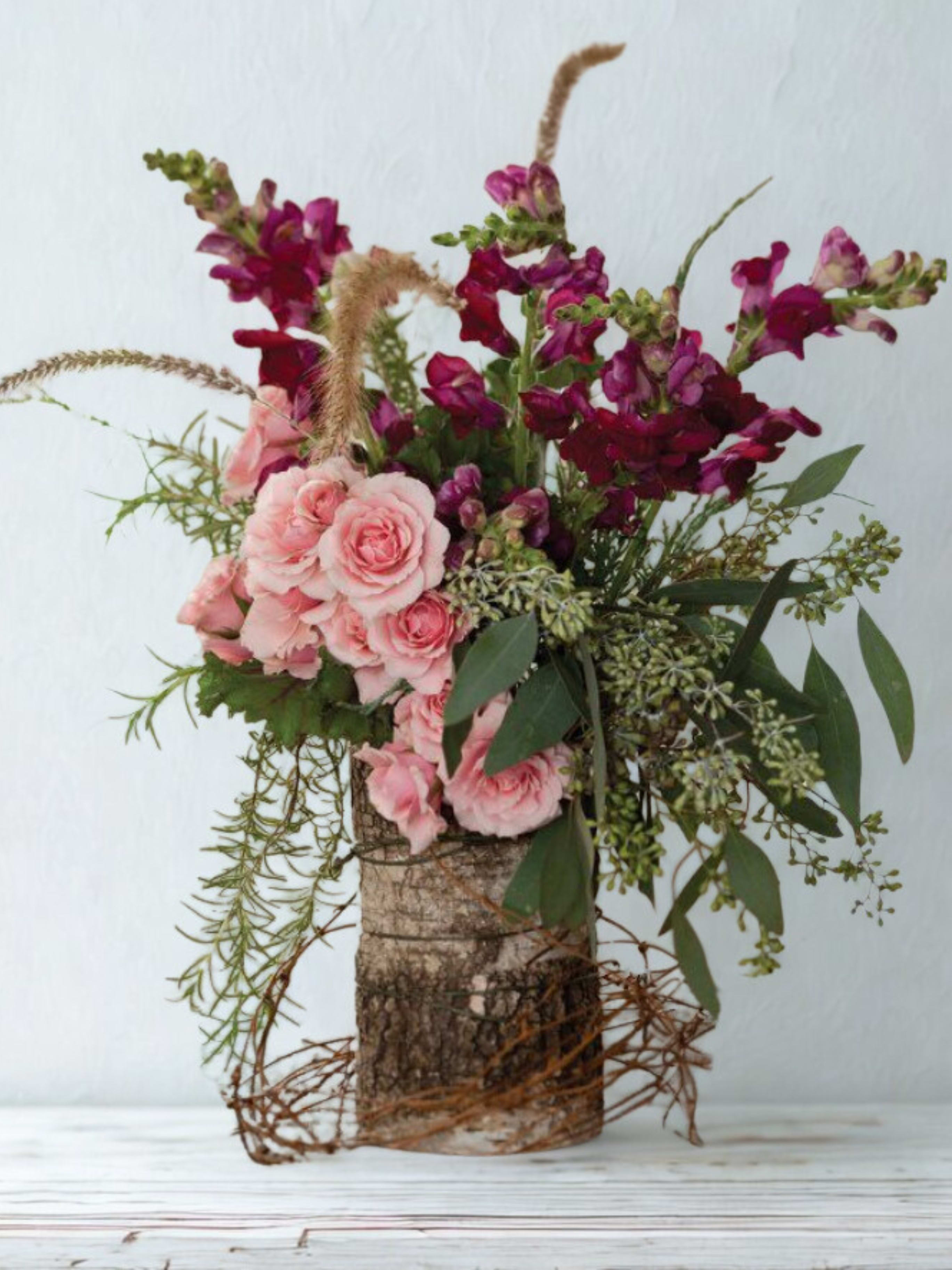Pink roses and magenta snapdragons in a rustic bark container
