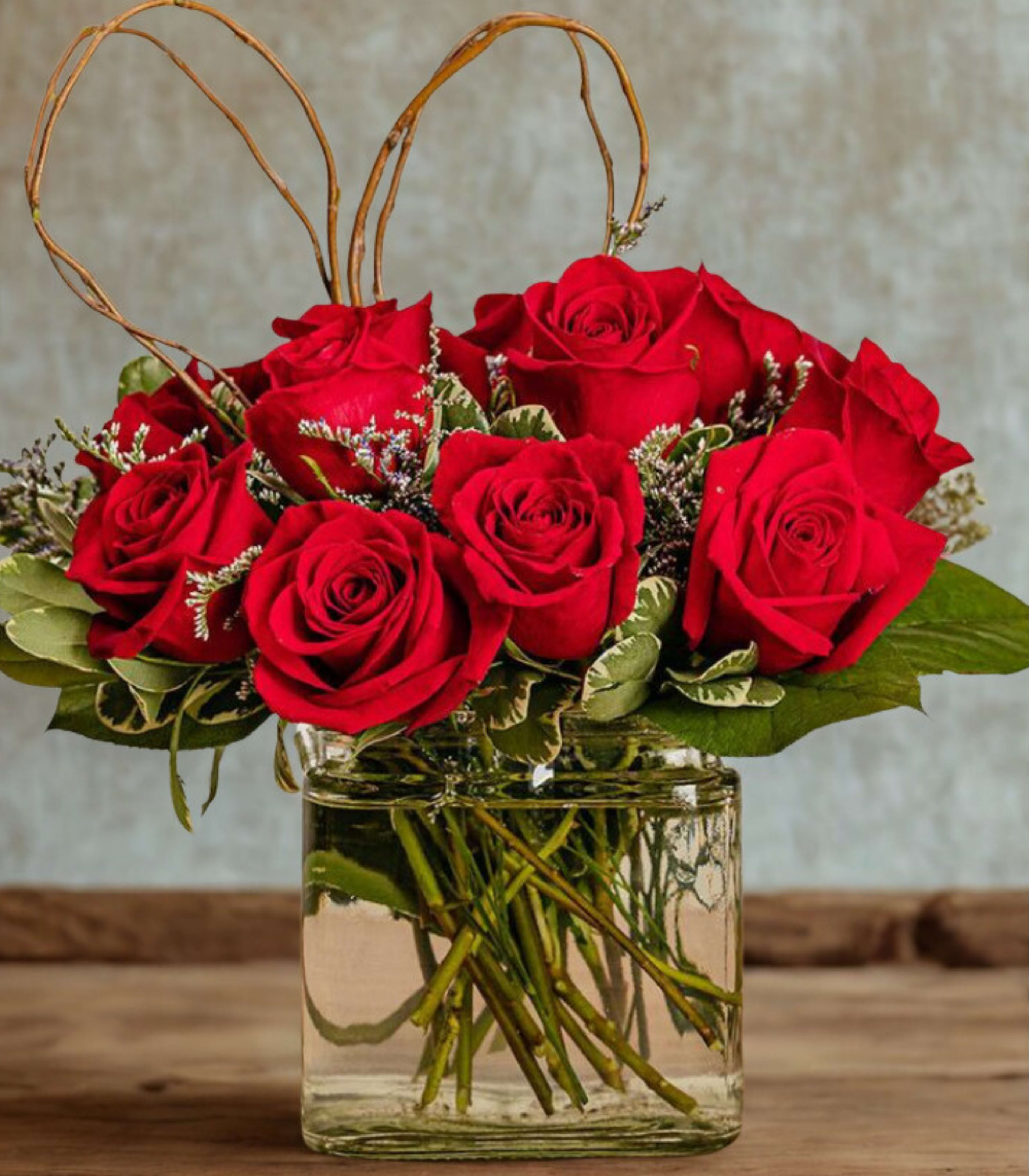 Red roses arranged in a clear glass vase with heart-shaped twigs