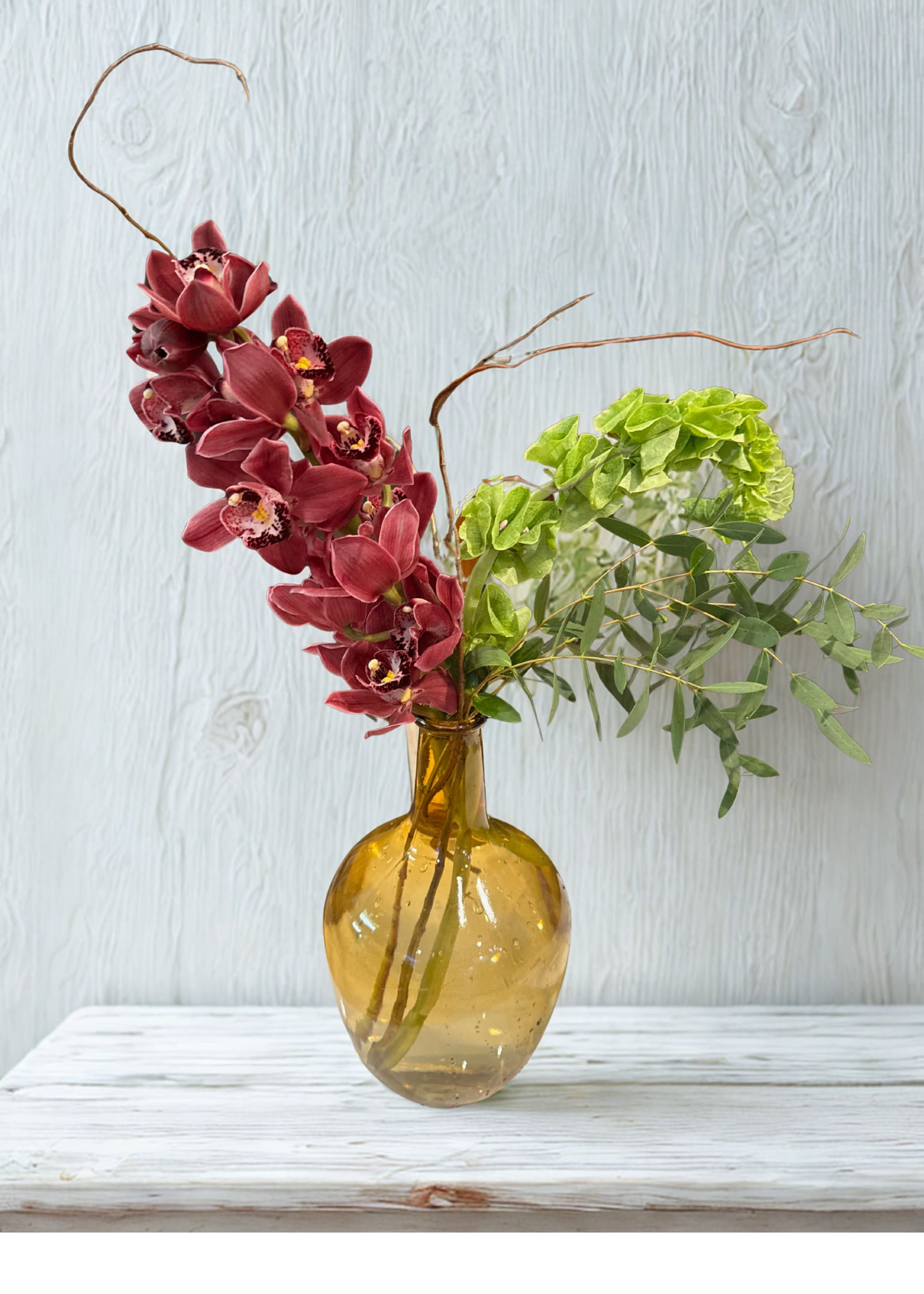 Burgundy orchids and green foliage in an amber glass vase