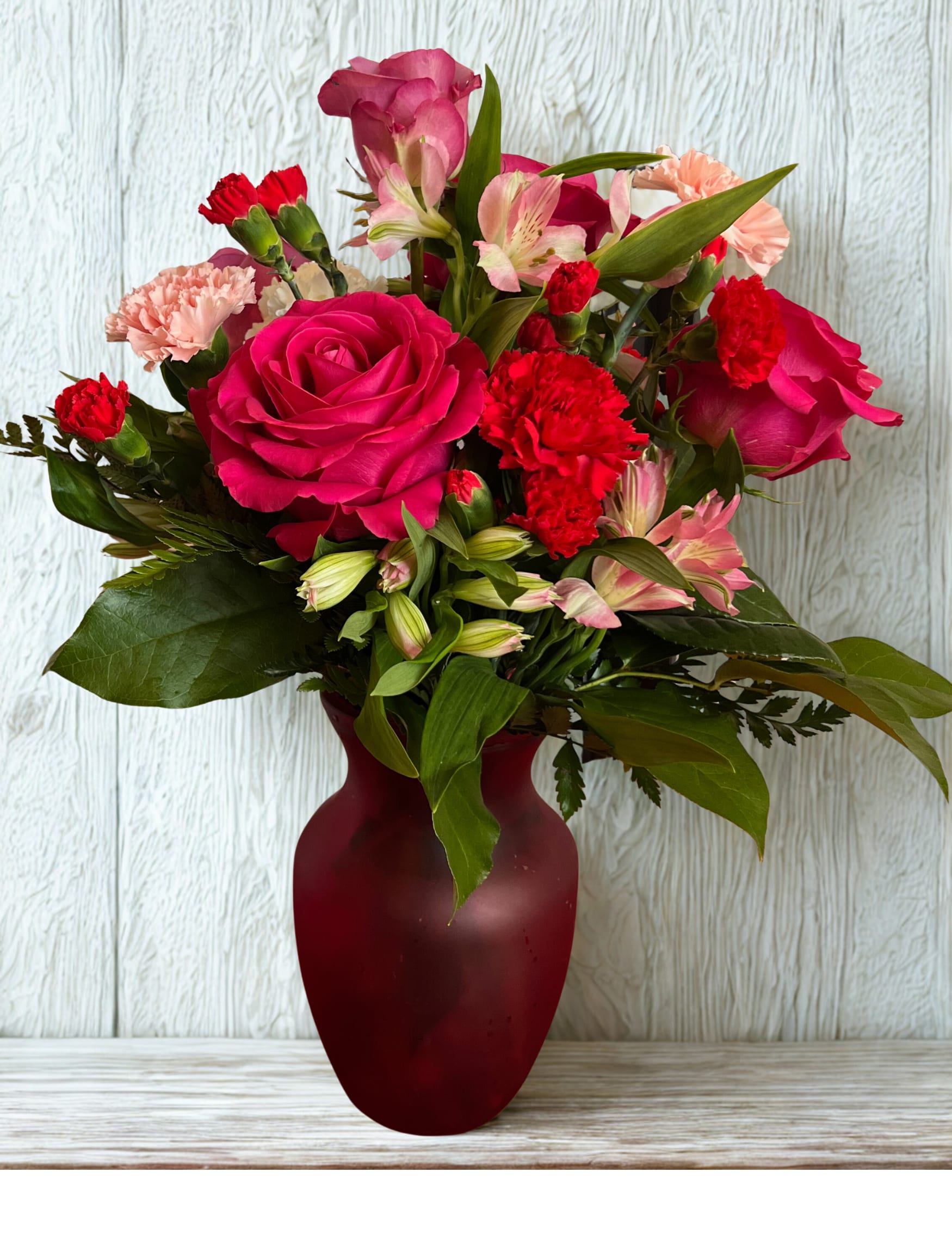 Pink roses and red carnations arranged in a burgundy vase